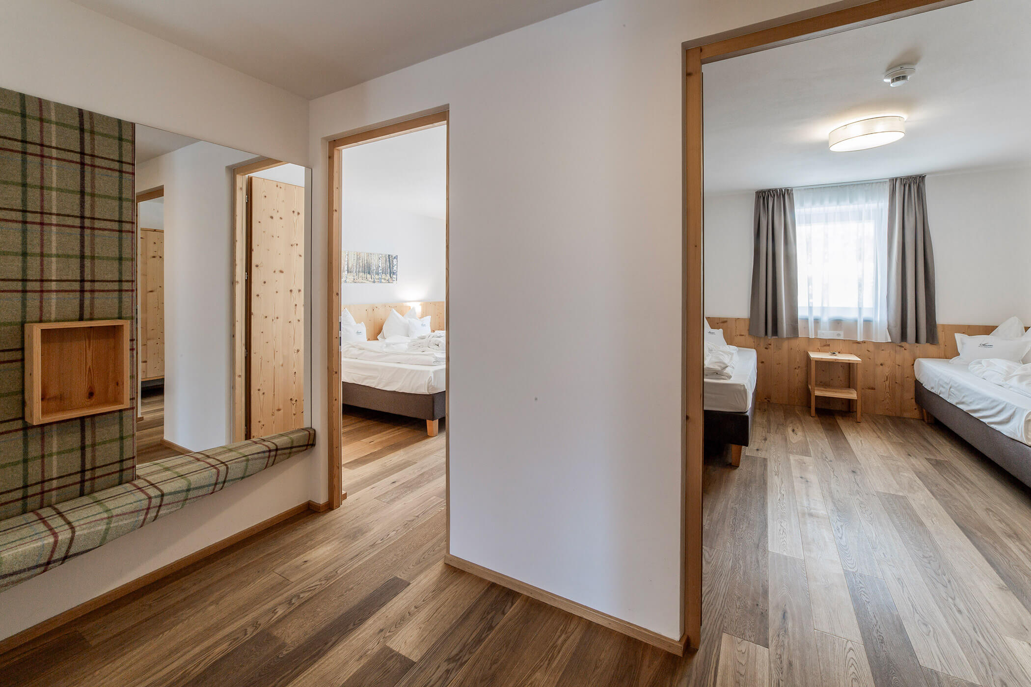 Suite d'albergo con due camere da letto, pavimenti in legno, pareti bianche e luce naturale che entra dalle ampie finestre. - Hotel Oberwiesen