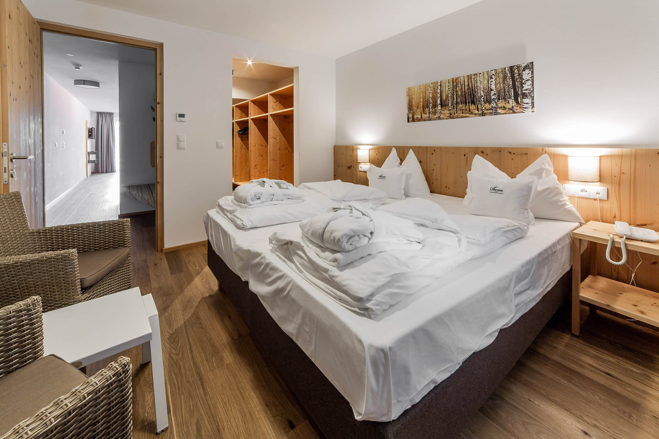 Camera d'albergo con un letto matrimoniale ben rifatto, pareti in legno, due sedie e un armadio a vista sullo sfondo. - Hotel Oberwiesen