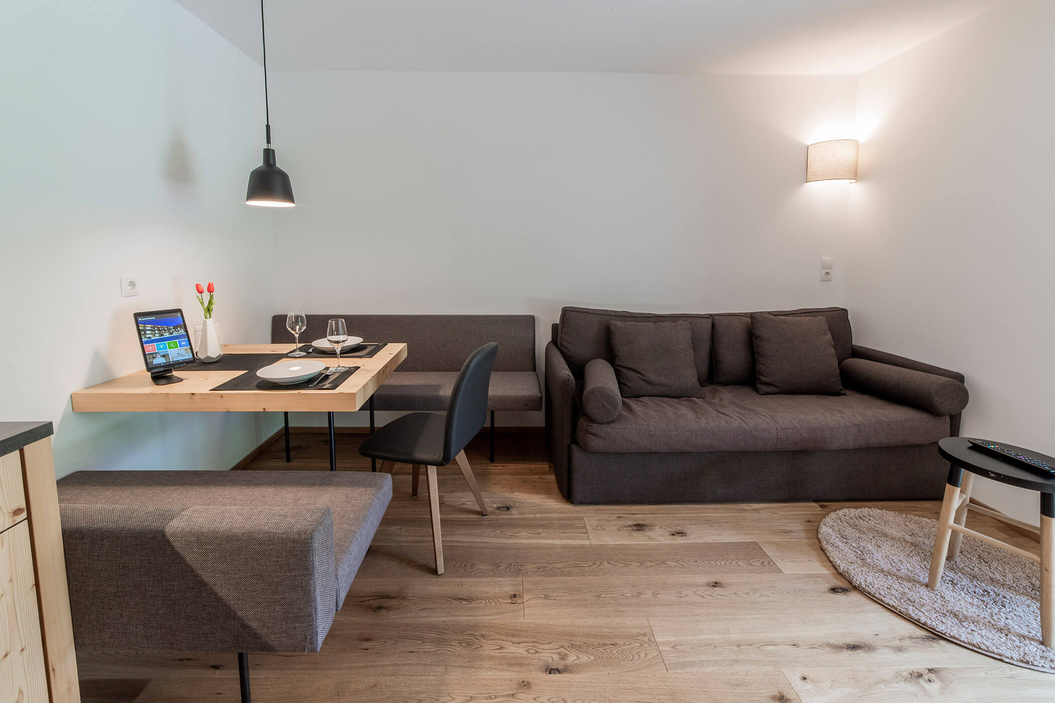 Soggiorno moderno con divano grigio, tavolo in legno, panca da pranzo e pavimento in parquet. - Hotel Oberwiesen
