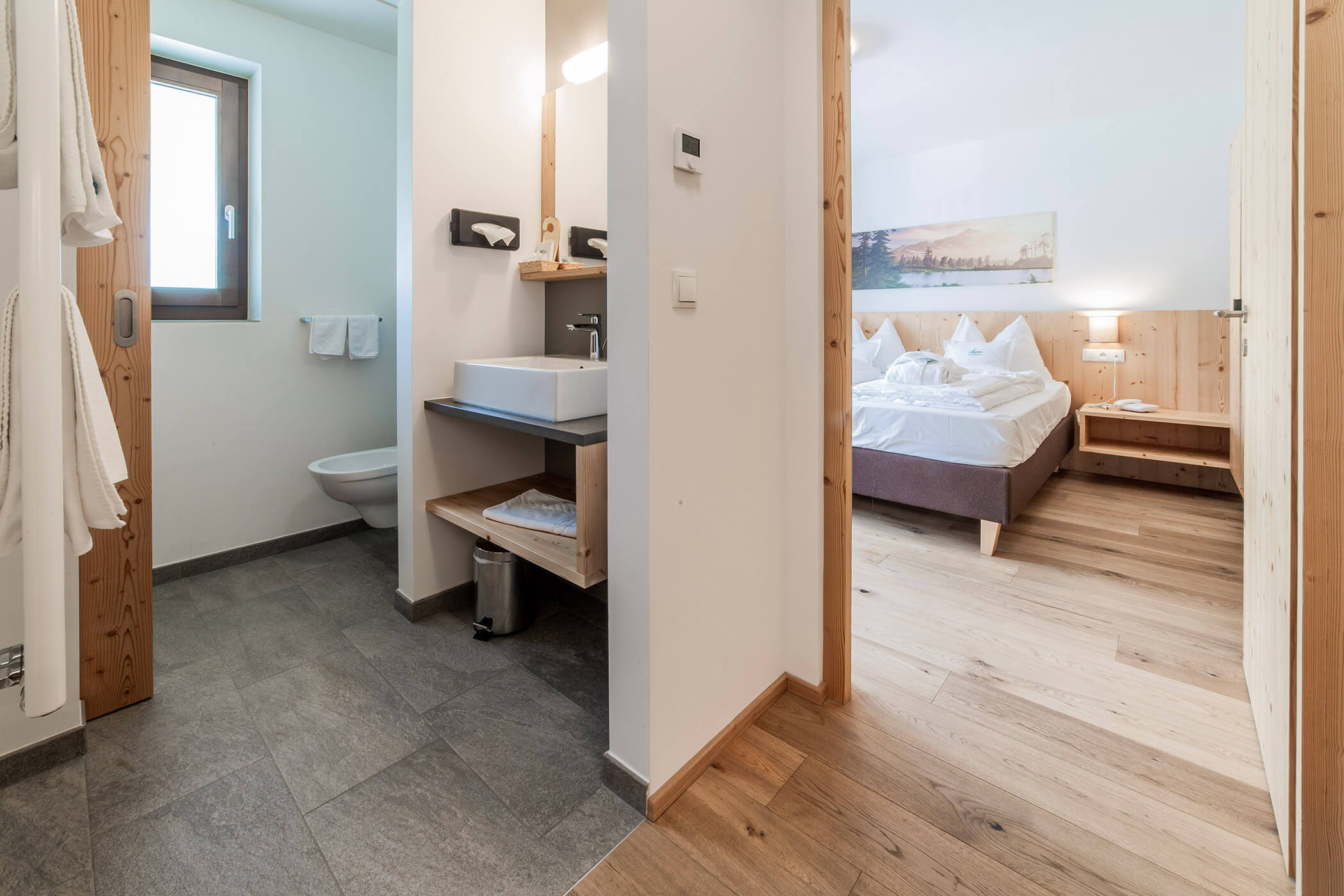 Camera d'albergo moderna con pavimenti in legno, bagno a vista, lavandino e letto ben rifatto nella camera da letto. - Hotel Oberwiesen