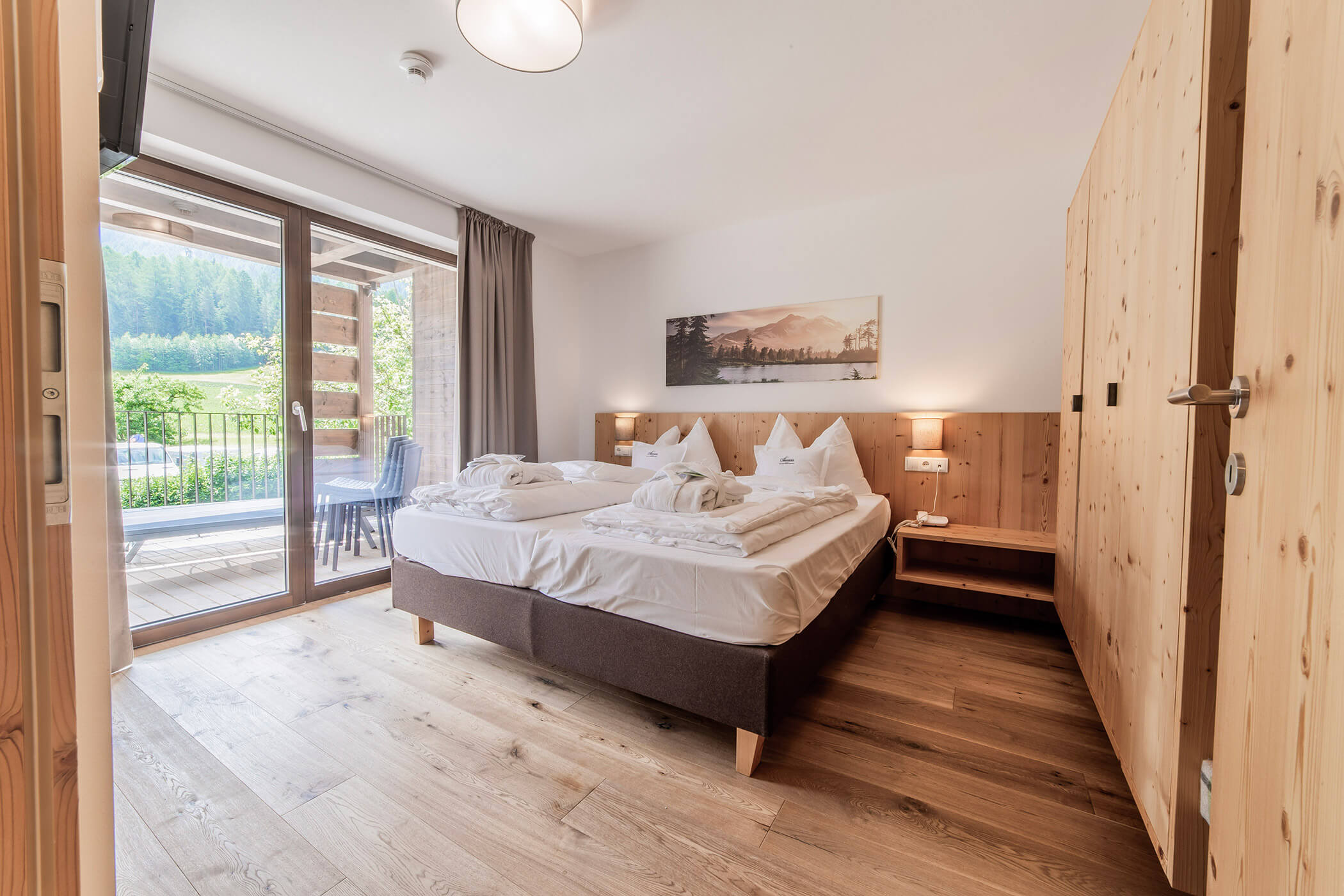 Luminosa camera d'albergo con letto matrimoniale, pavimento in legno, balcone con vista e un panorama naturale raffigurato sulla parete sopra il letto. - Hotel Oberwiesen