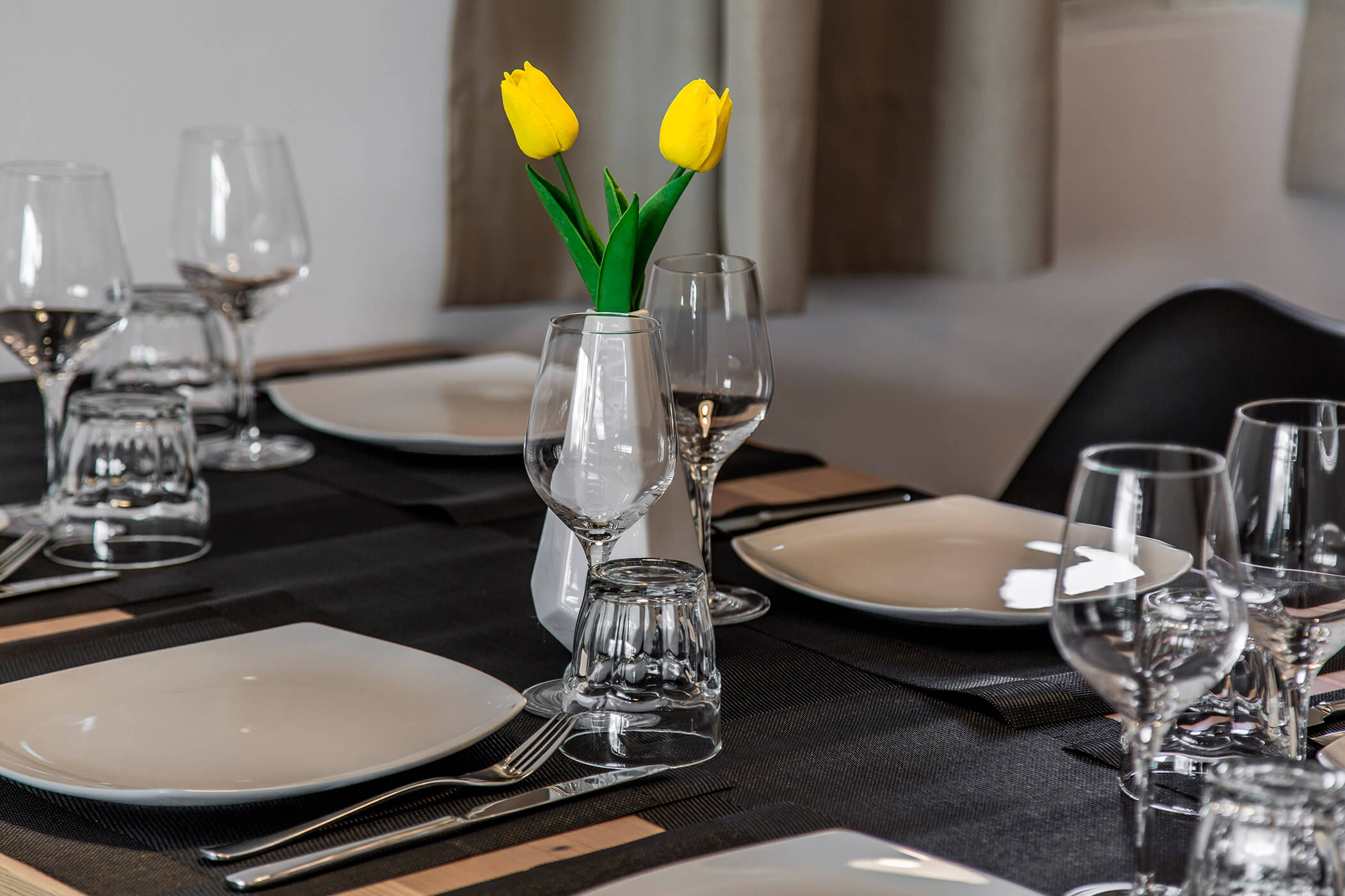 Eine elegante Tischdekoration mit weißen Tellern, Weingläsern und gelben Tulpen in einer Vase als Tischschmuck. - Hotel Oberwiesen
