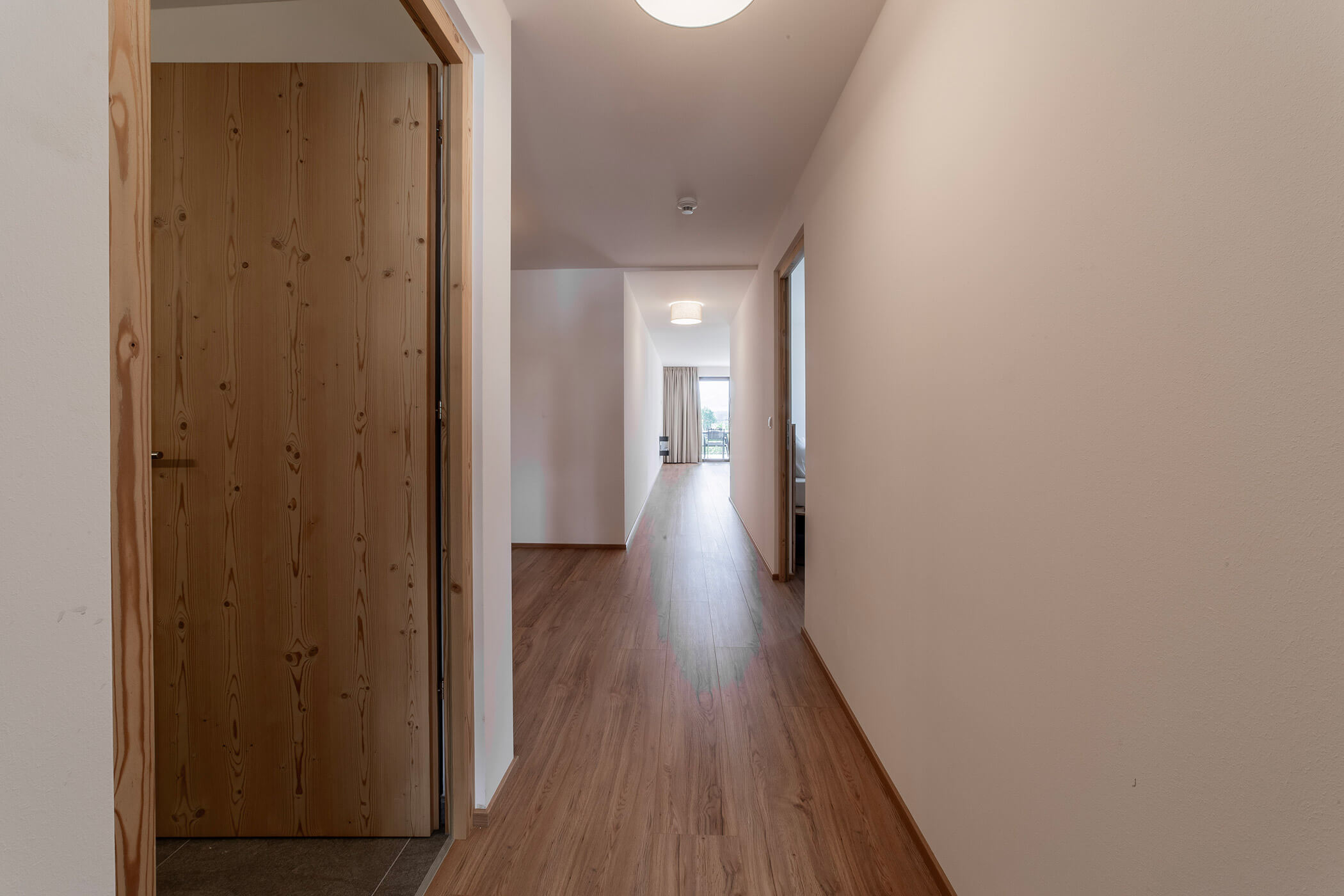 Un lungo corridoio con pavimento in legno, una porta sulla sinistra e la luce che filtra da una finestra in fondo. - Hotel Oberwiesen