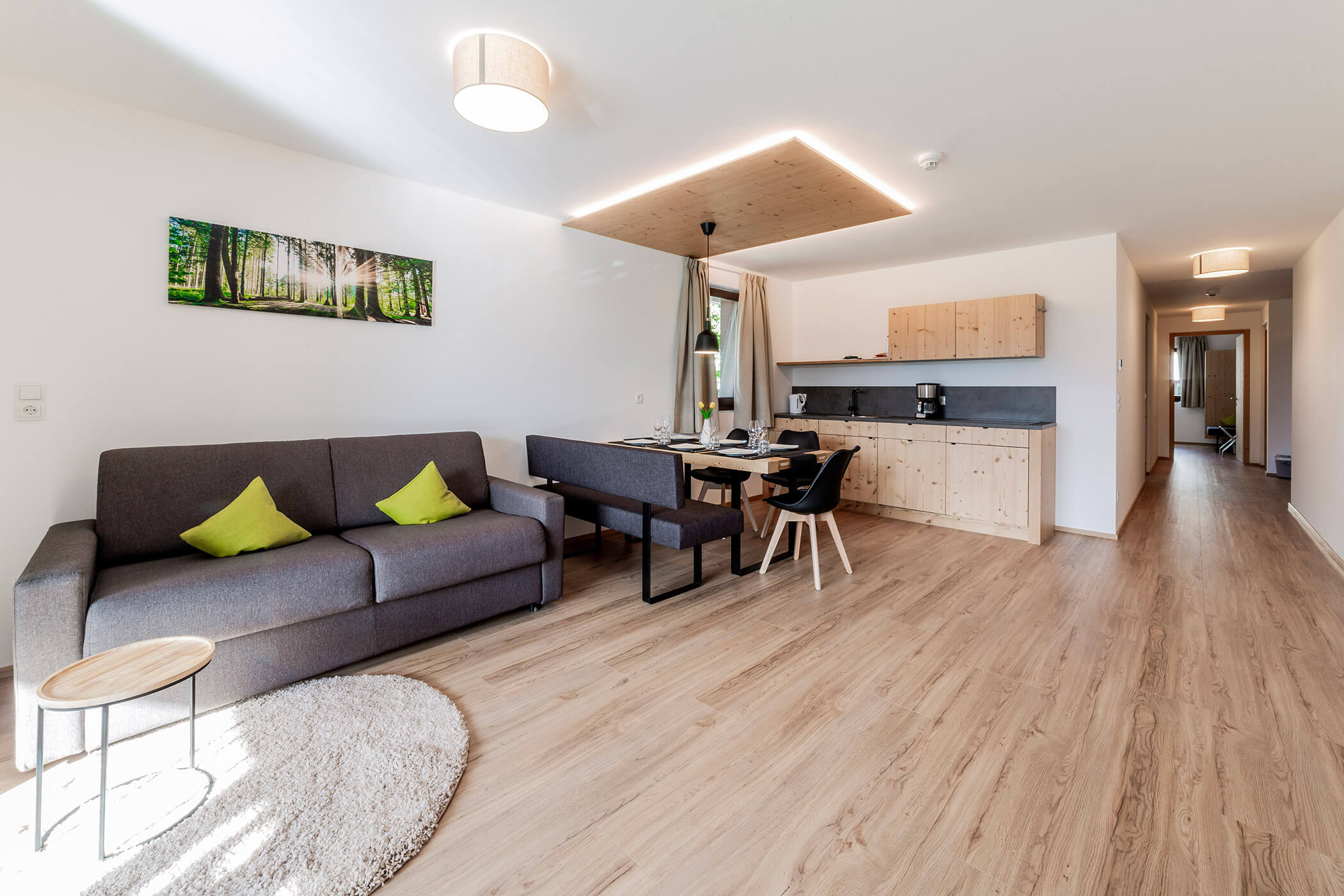 Moderno soggiorno-cucina a pianta aperta con pavimento in legno, tonalità neutre e cuscini decorativi verdi. - Hotel Oberwiesen