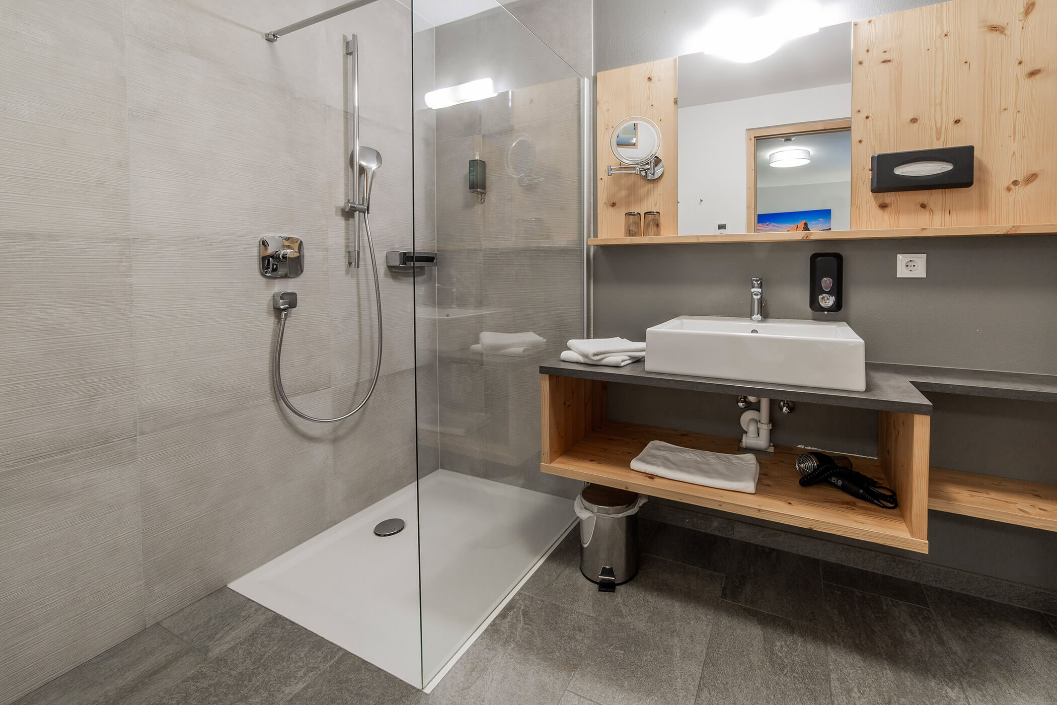 Bagno moderno con cabina doccia, lavabo sospeso, mensole in legno, asciugamani e uno specchio sopra. - Hotel Oberwiesen