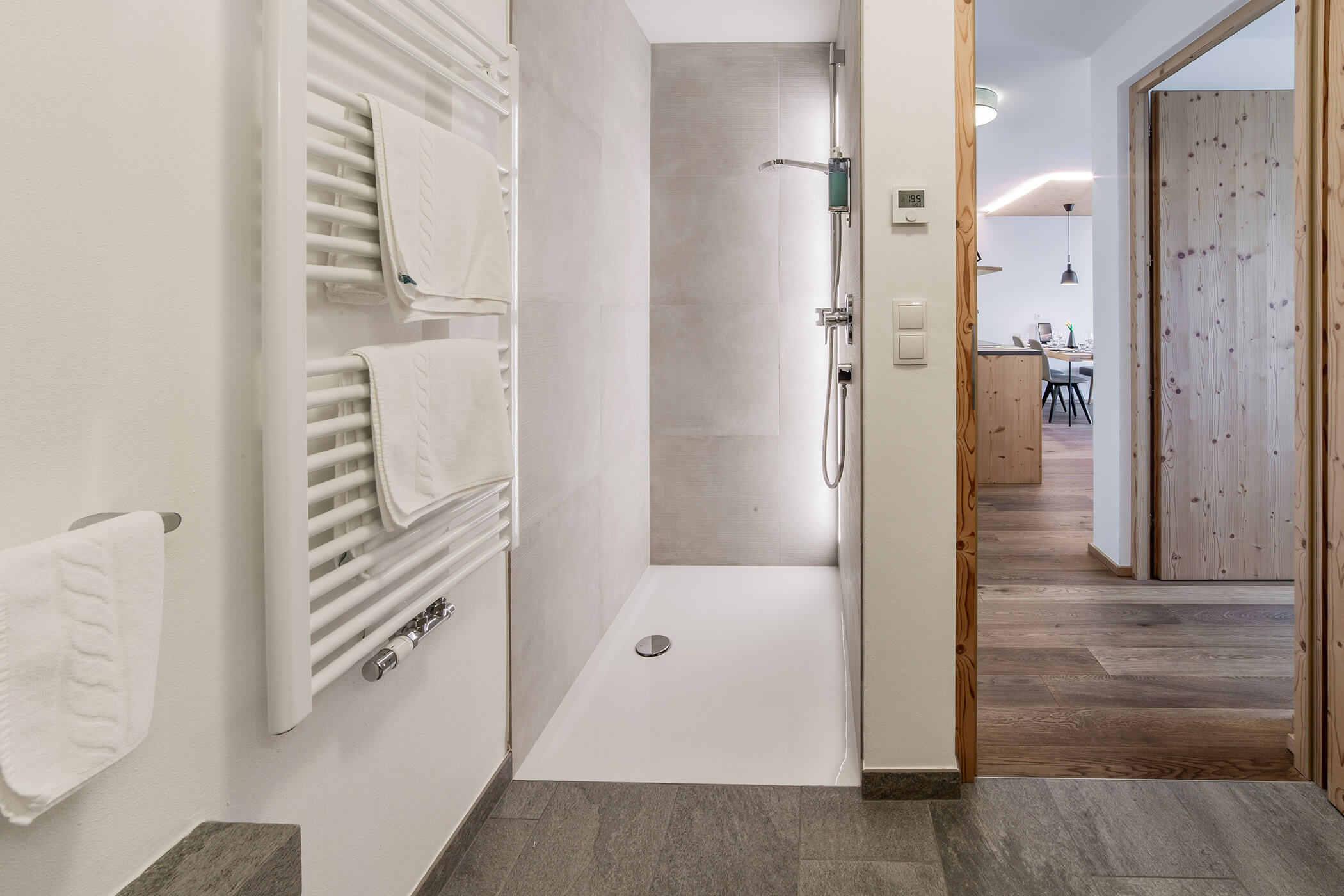 Bagno moderno con cabina doccia, asciugamani bianchi e vista sulla zona giorno con pavimento in legno. - Hotel Oberwiesen