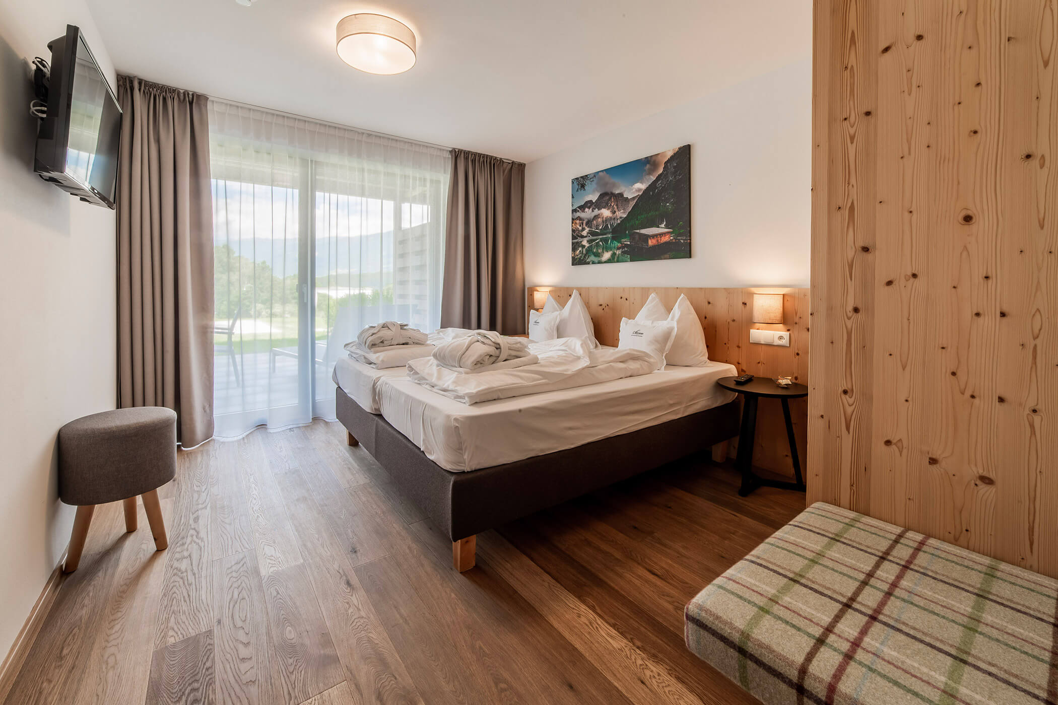 Camera d'albergo luminosa con due letti, una TV a parete, un'ampia finestra e dettagli in legno. - Hotel Oberwiesen
