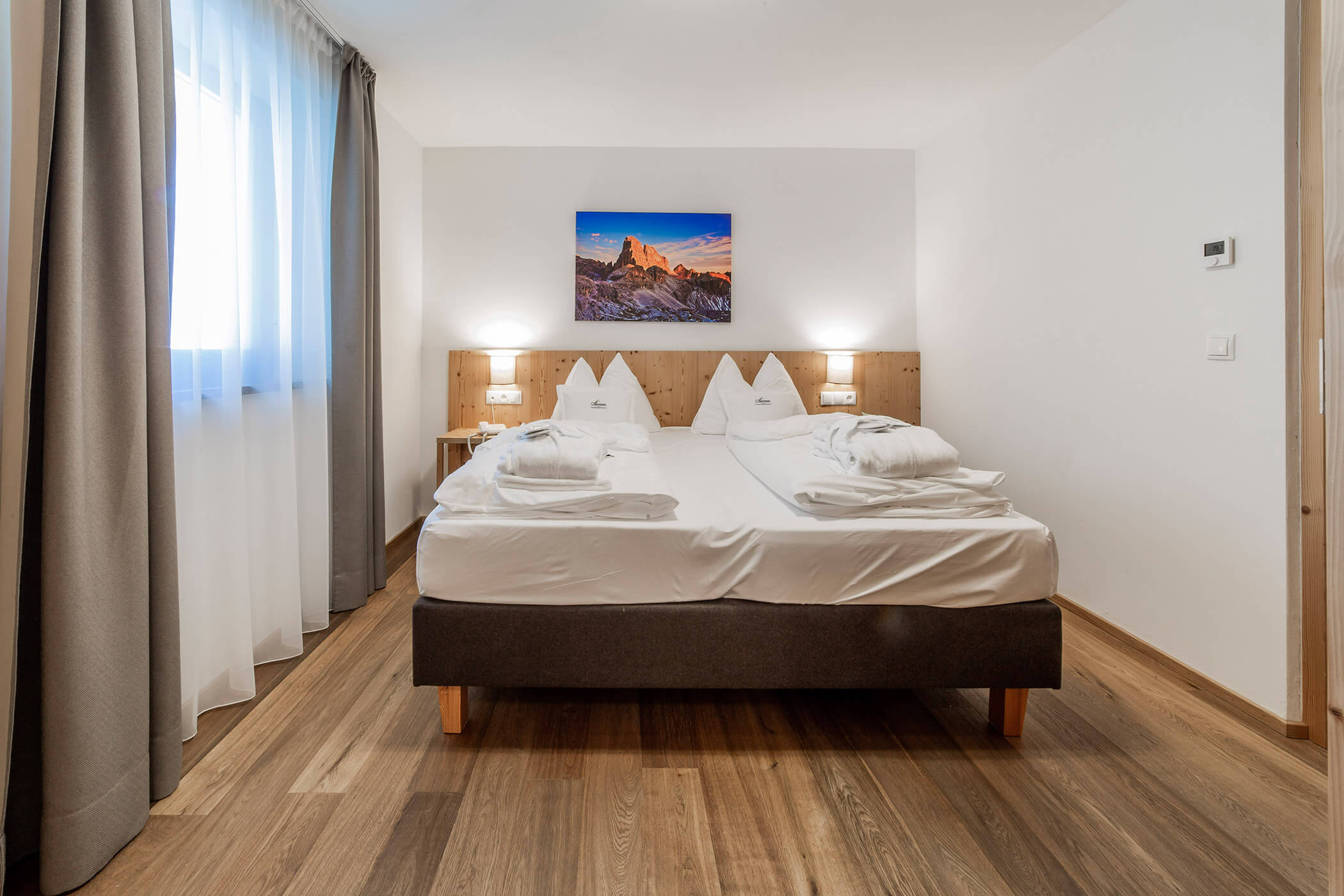 Camera d'albergo moderna con letto matrimoniale, pavimento in legno, lampade da comodino e una foto di montagna appesa alla parete. - Hotel Oberwiesen