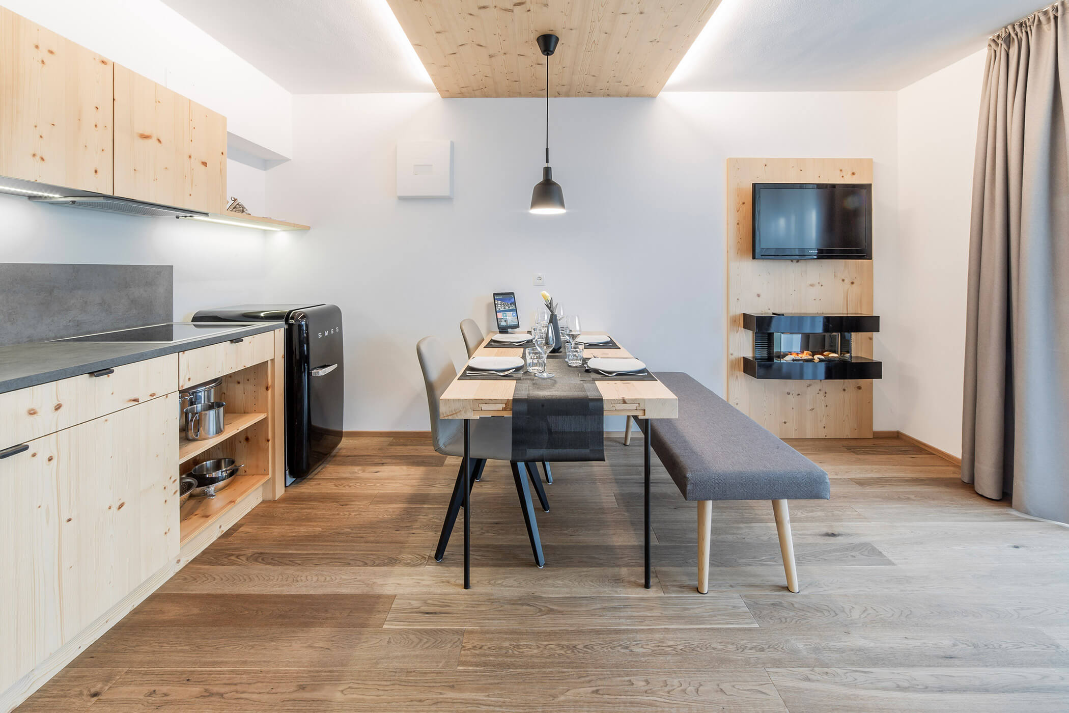 Moderner Küchen-Essbereich mit Holzschränken, einer Sitzbank, einem schwarzen Kühlschrank und einem an der Wand montierten Fernseher. - Hotel Oberwiesen