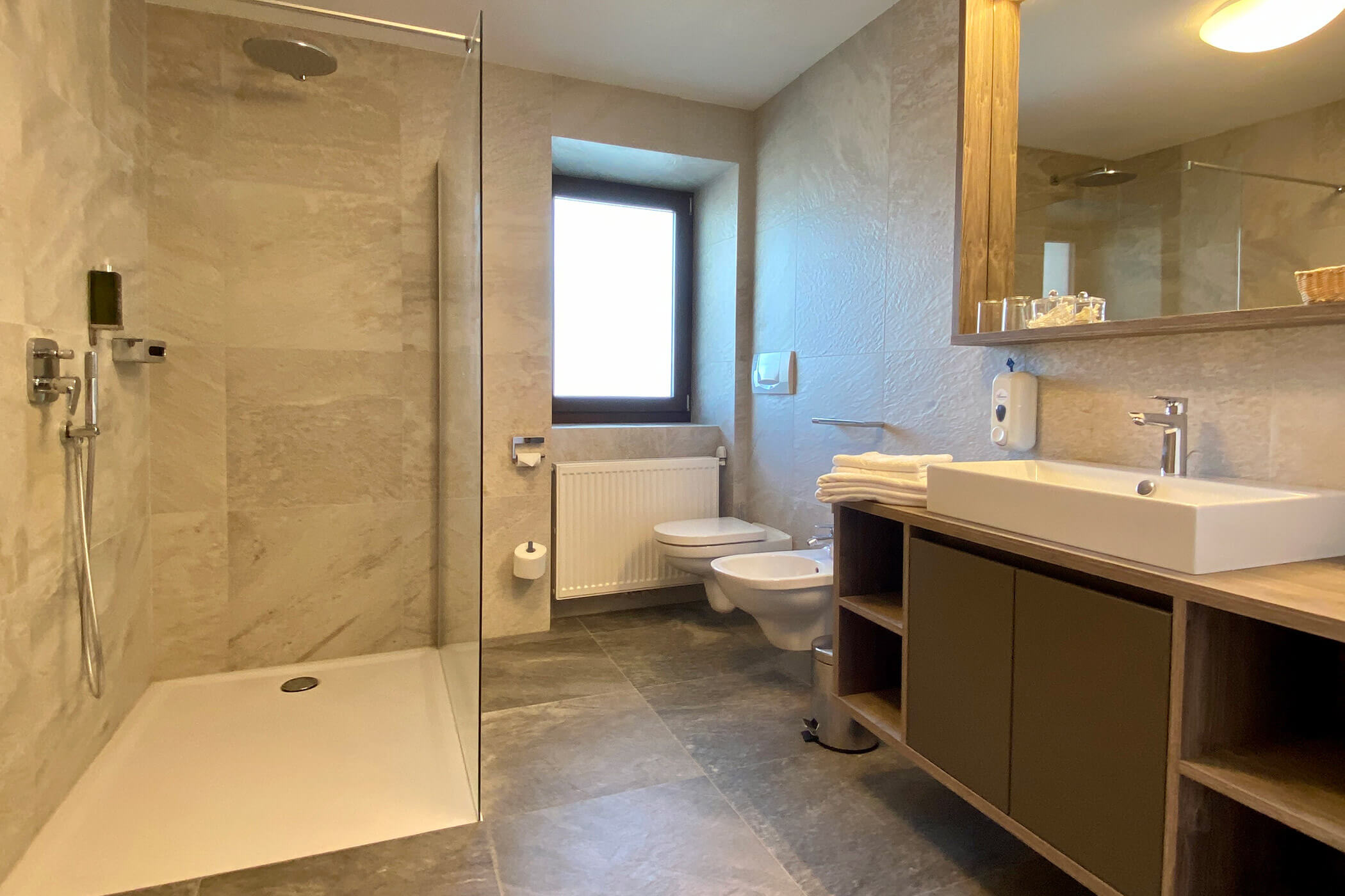 Bagno moderno con cabina doccia, lavabo, WC, bidet, ampio specchio e piastrelle beige. - Hotel Oberwiesen