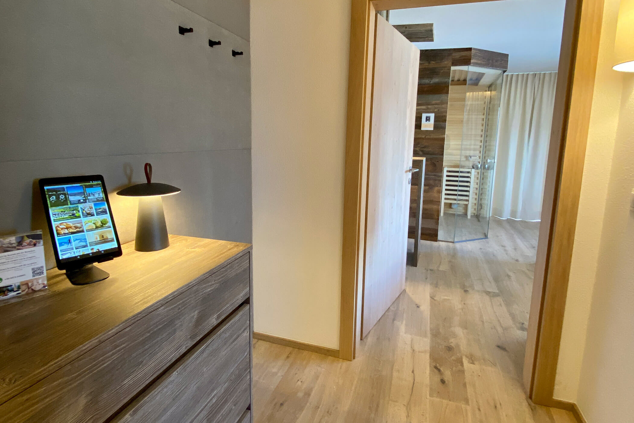 Un tablet appoggiato su una cassettiera di legno in un corridoio, con vista su una camera da letto e un bagno in stile moderno. - Hotel Oberwiesen