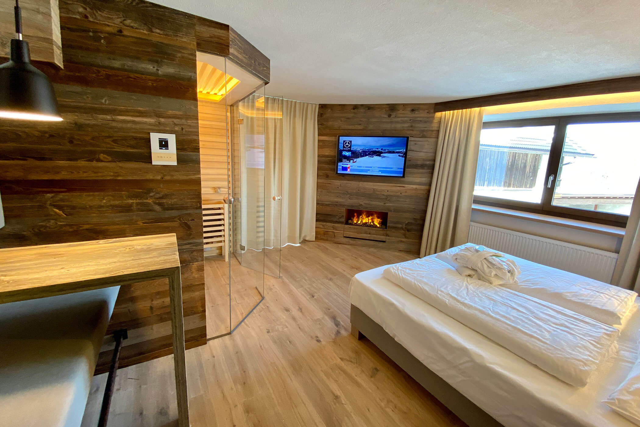 Camera d'albergo moderna con dettagli in legno, letto matrimoniale, caminetto, TV, ampia finestra e box doccia in vetro. - Hotel Oberwiesen