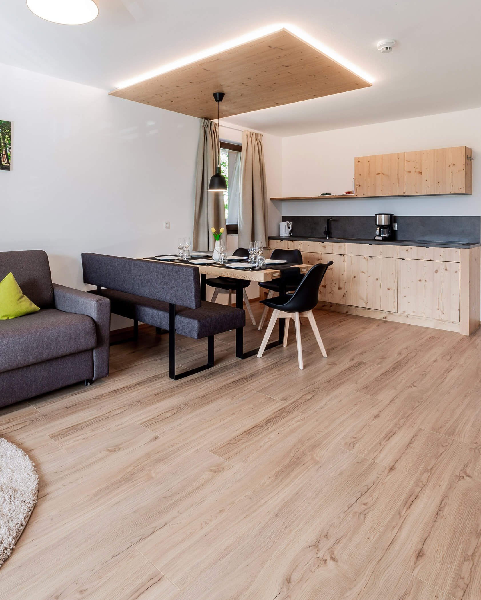 Modern kitchen and dining area with wooden floors, gray sofa, and light wood cabinets. - Hotel Oberwiesen