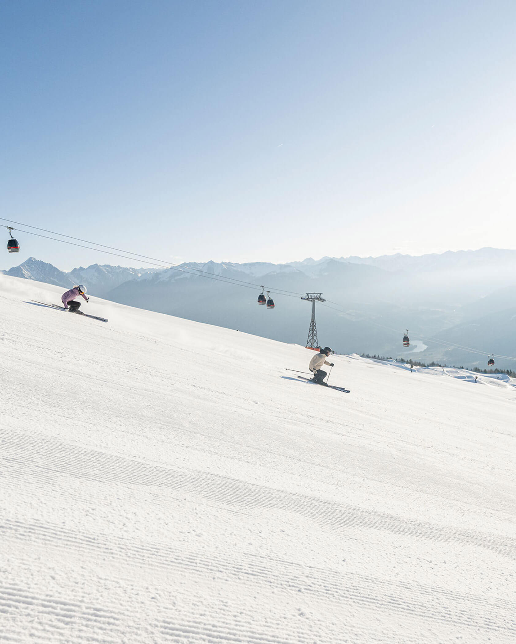 Drei Skifahrer fahren auf einem sonnigen, verschneiten Hang bergab, im Hintergrund sind Skilifte und Berge zu sehen. - Hotel Oberwiesen