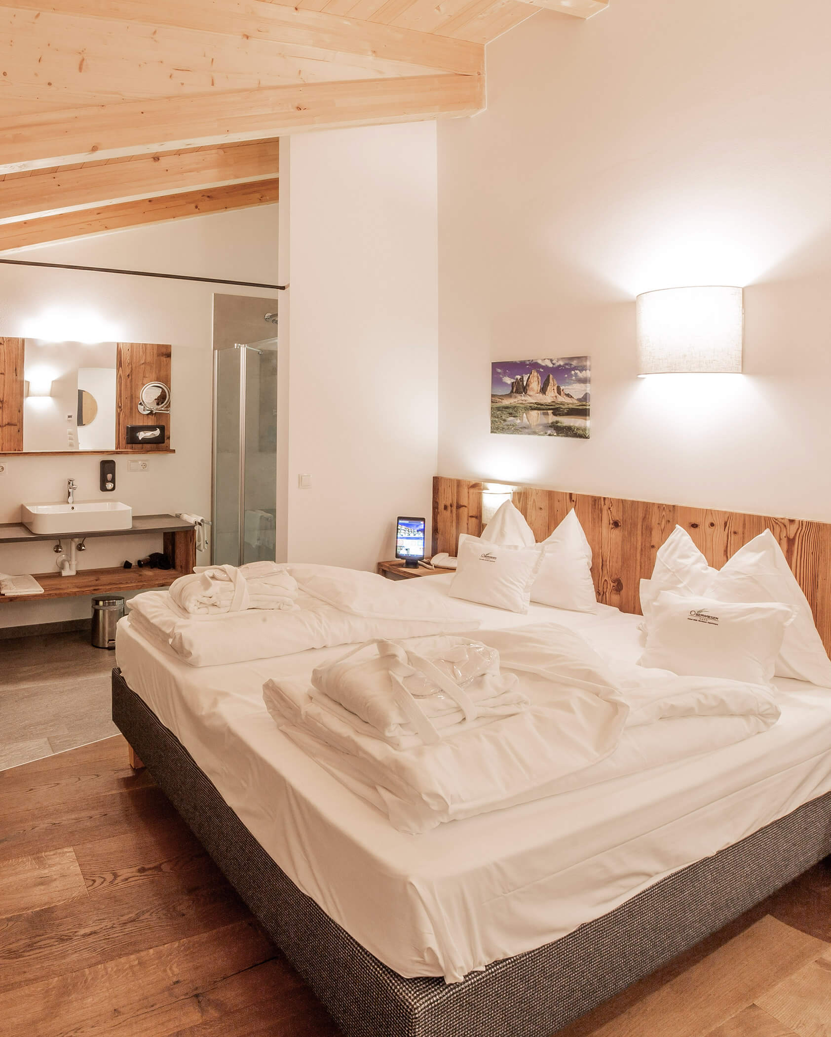 Cozy hotel room with a double bed, wood accents, tidy linens, and an open bathroom area in the background. - Hotel Oberwiesen