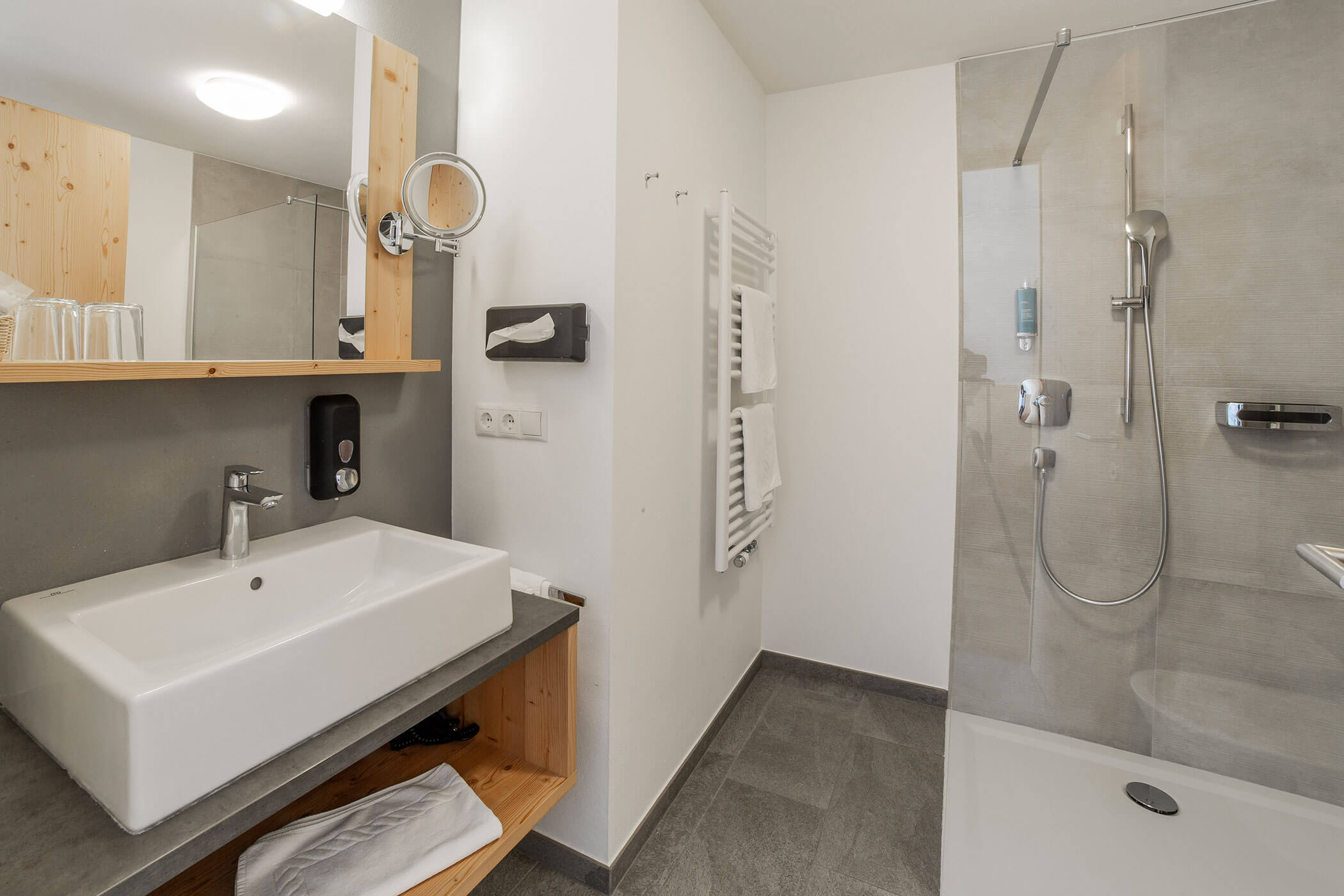 Bagno moderno con lavabo, specchio, asciugamani e cabina doccia con parete divisoria in vetro. - Hotel Oberwiesen