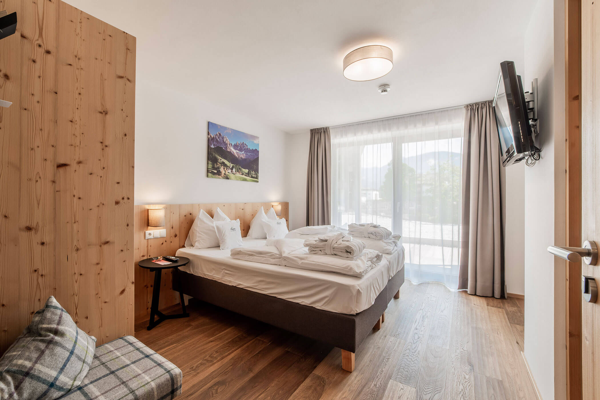 Camera d'albergo luminosa con letto matrimoniale, TV a parete, set di accappatoi, ampia finestra e dettagli in legno. - Hotel Oberwiesen