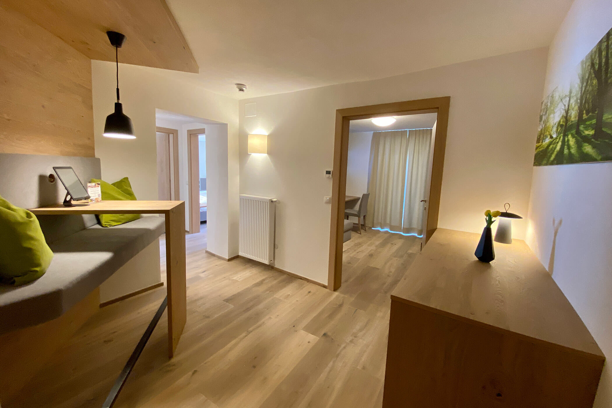 Moderno ingresso con pavimento in legno, panca a incasso, scrivania e vista su una stanza con tende e tavolo. - Hotel Oberwiesen