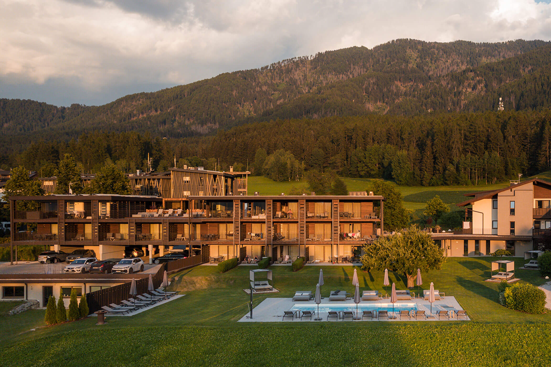 Ein Hotel mit Balkonen und einem Außenpool inmitten eines grünen Tals, mit bewaldeten Bergen im Hintergrund. - Hotel Oberwiesen