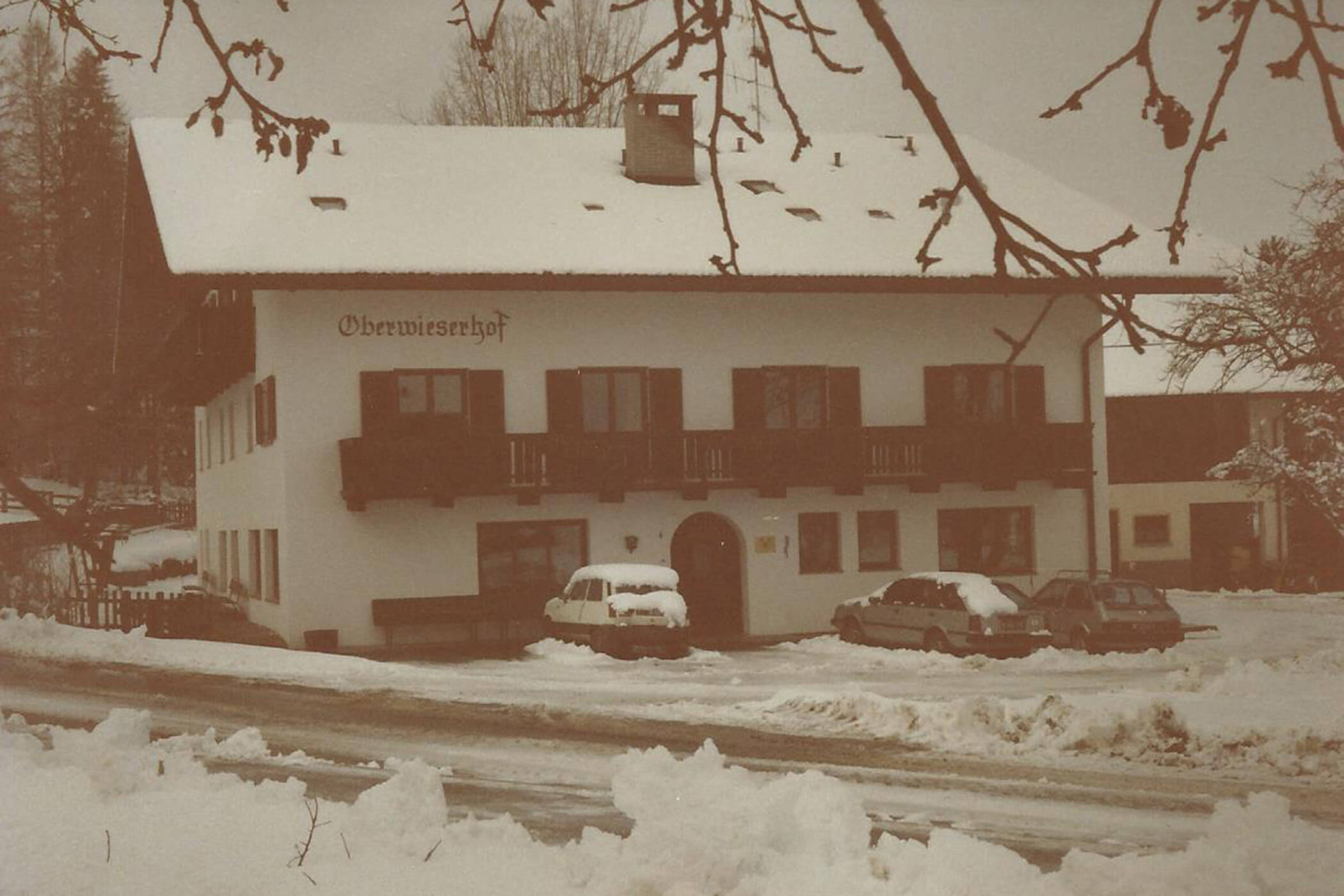Ein schneebedecktes Gebäude mit der Aufschrift „Oberwiserhof“ und geparkten Autos, aufgenommen an einem Wintertag. - Hotel Oberwiesen