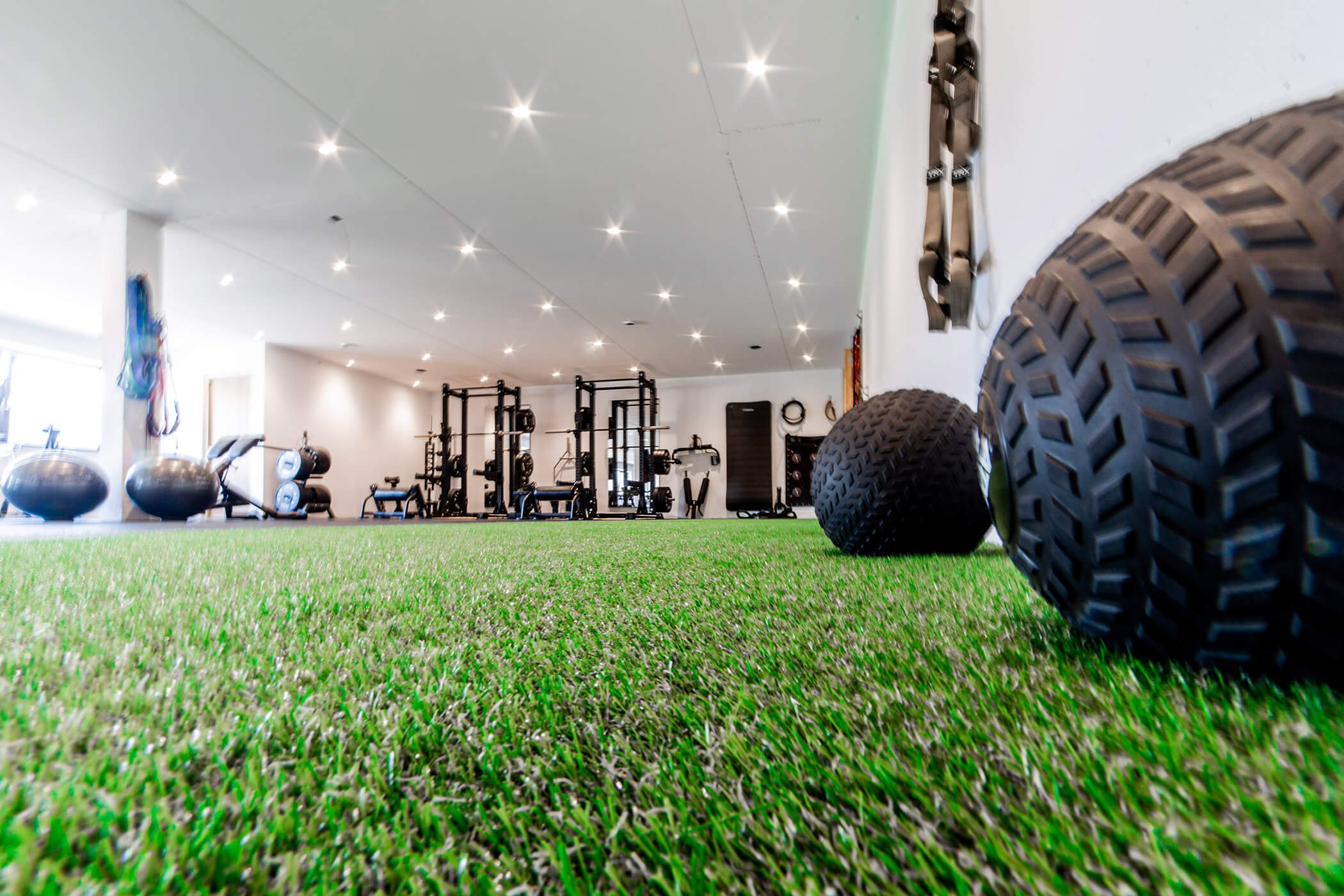 Fitnessstudio mit Kunstrasenboden, Medizinbällen, Hantelständern und Fitnessgeräten unter hellen Deckenleuchten. - Hotel Oberwiesen