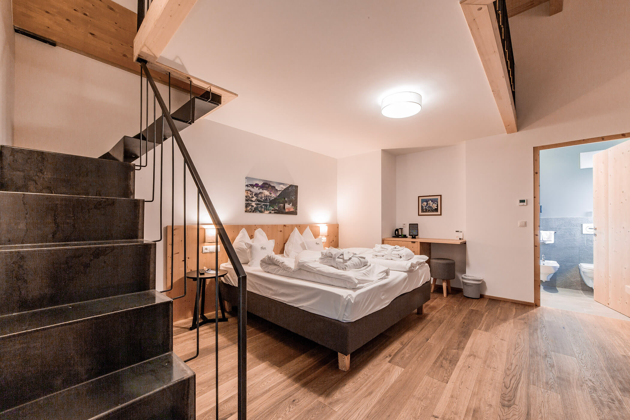 Camera d'albergo moderna con pavimenti in legno, letto matrimoniale, scala e bagno visibile attraverso la porta aperta. - Hotel Oberwiesen