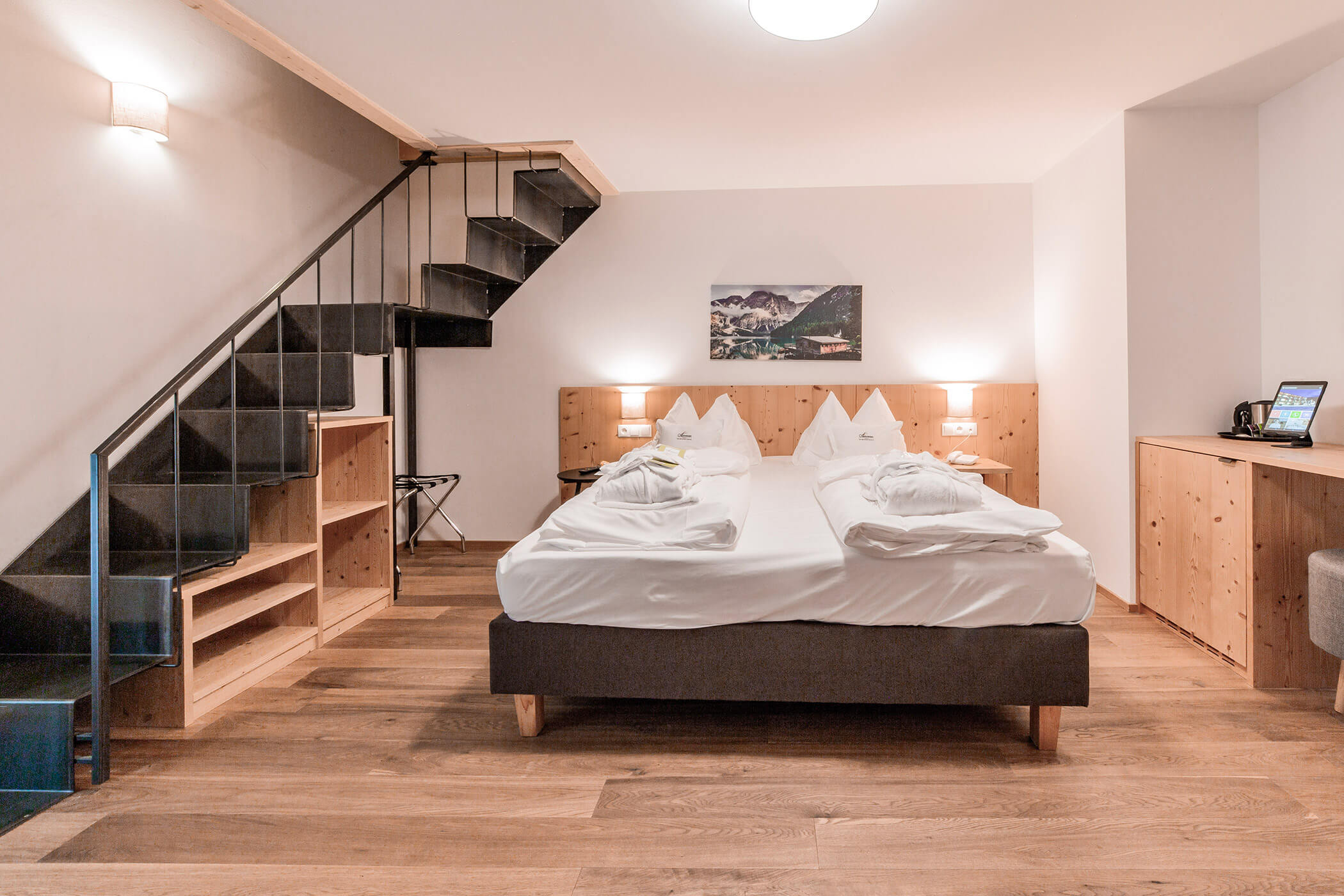 Camera d'albergo moderna con letto matrimoniale, mobili in legno, scala a vista e un quadro raffigurante un paesaggio appeso alla parete. - Hotel Oberwiesen