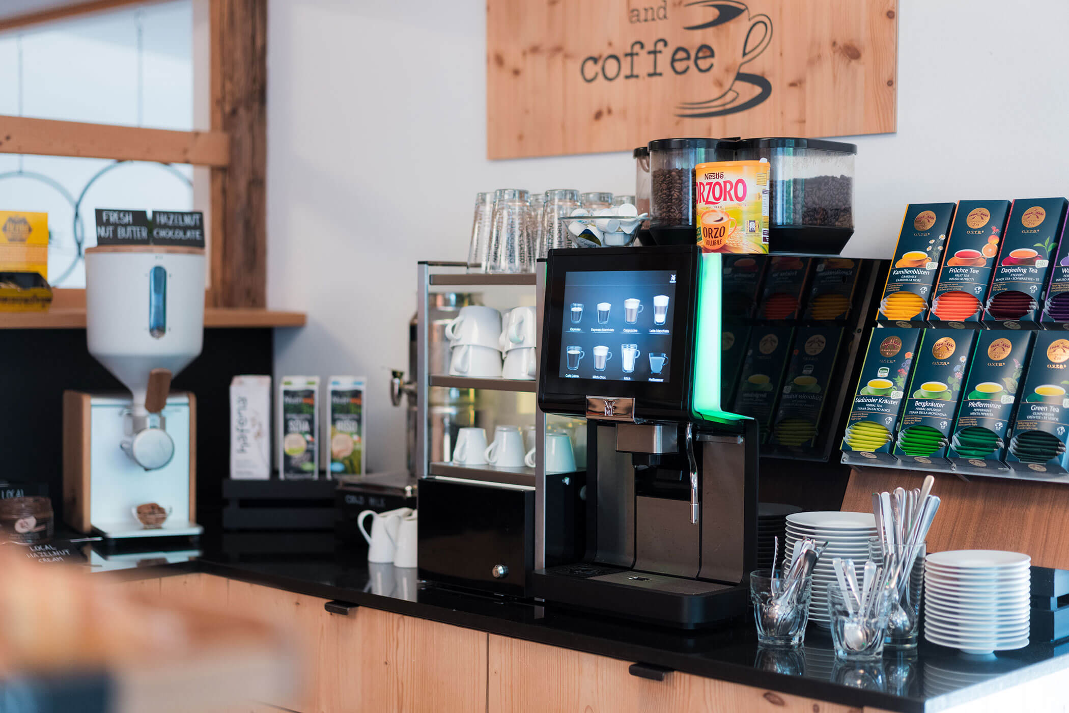 Angolo caffè con macchina da caffè, tazze, cialde, bicchieri e posate disposti in modo ordinato su un bancone. - Hotel Oberwiesen