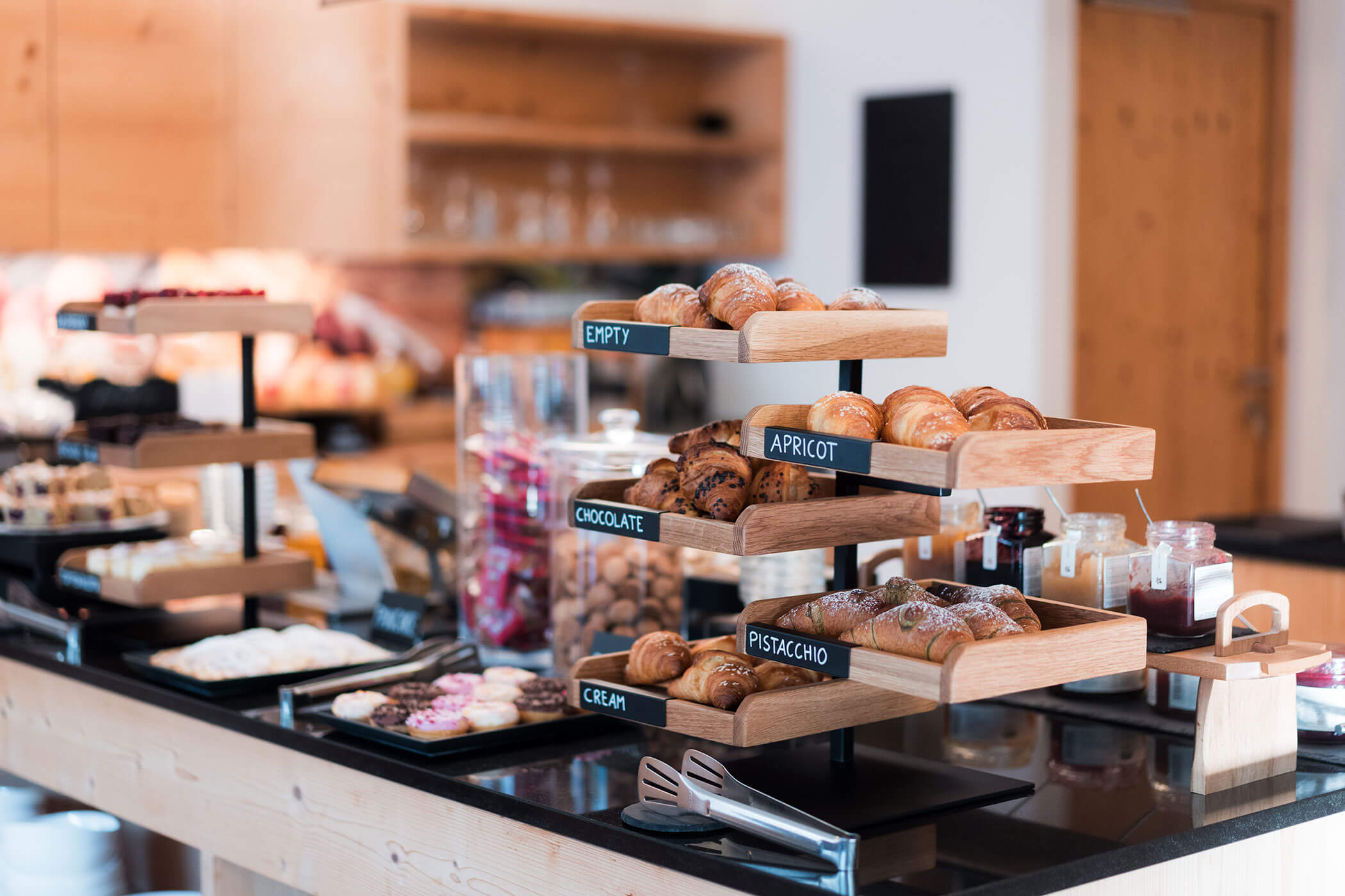 Angolo pasticceria self-service con vassoi etichettati contenenti croissant e prodotti da forno assortiti in una cucina moderna. - Hotel Oberwiesen