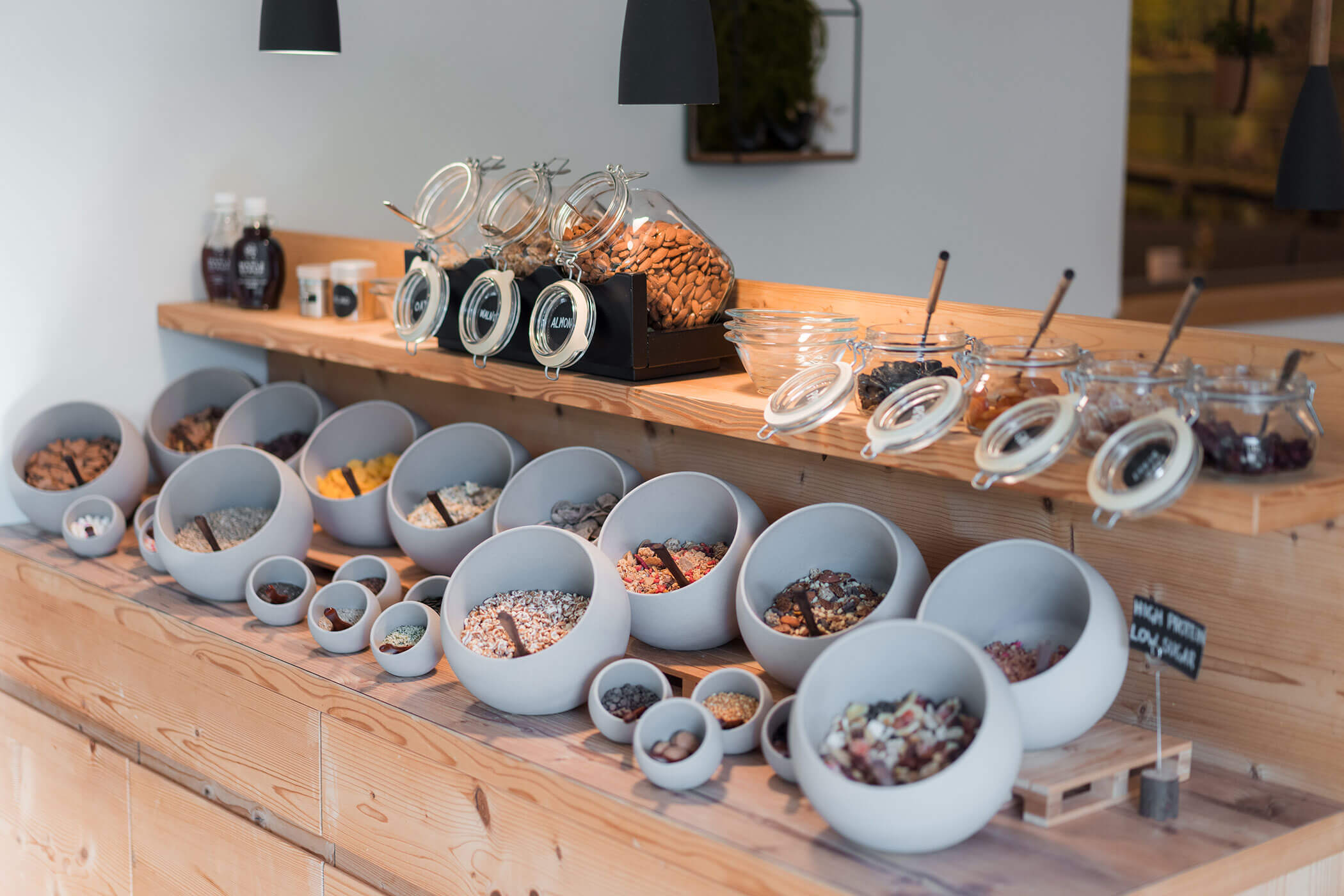 Vari cereali per la colazione, frutta secca e frutta essiccata in ciotole e barattoli grigi su un bancone di legno. - Hotel Oberwiesen