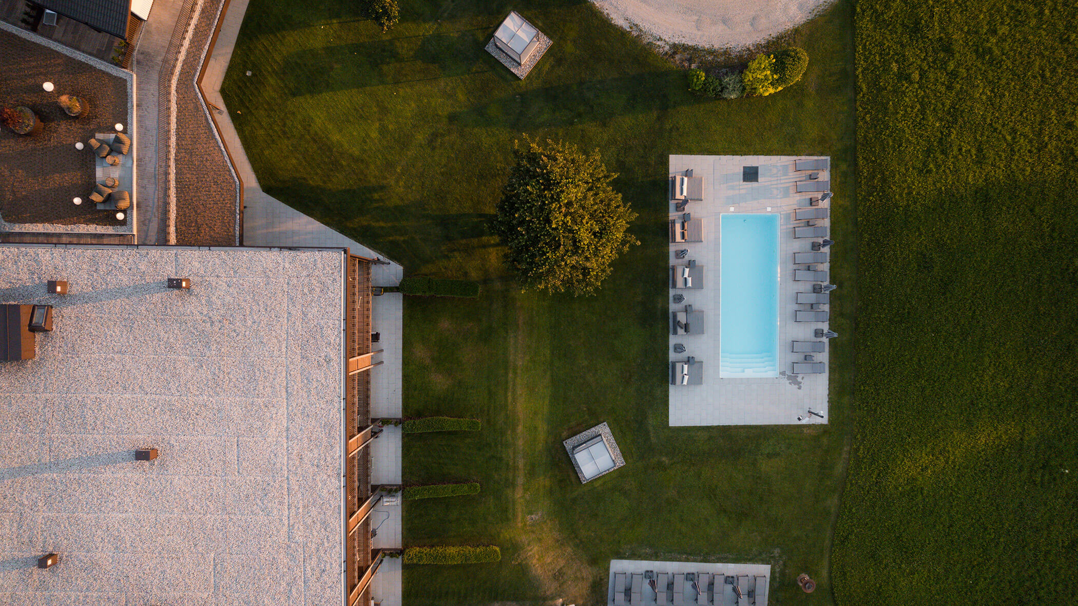 Aerial view of a building, a rectangular pool, lounge chairs, green lawn, and trees. - Hotel Oberwiesen