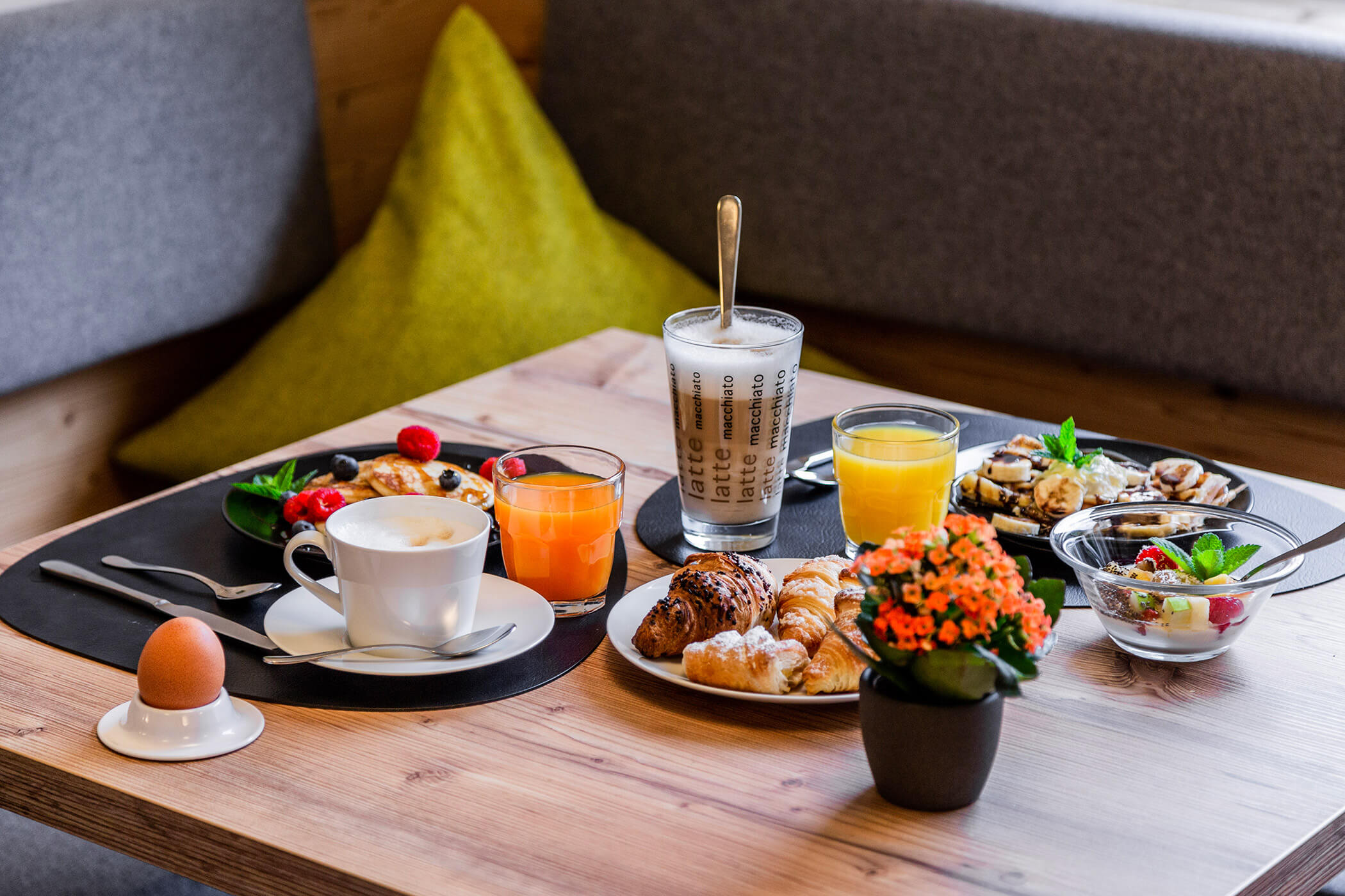 Breakfast table with coffee, juice, pastries, an egg, fruit, yogurt parfait, and a small orange potted flower. - Hotel Oberwiesen