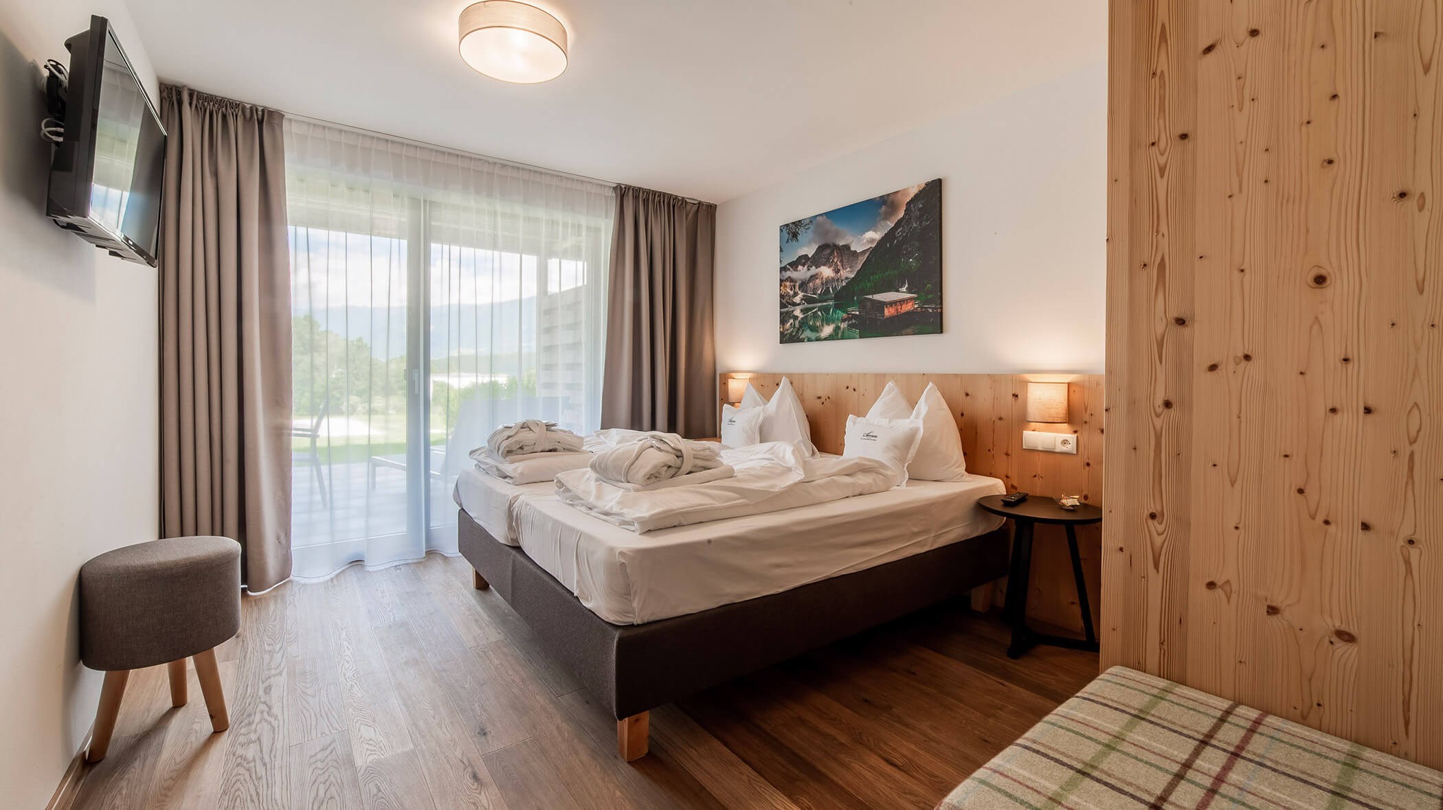 Modern hotel room with twin beds, wooden decor, a window with curtains, and a wall-mounted TV. - Hotel Oberwiesen