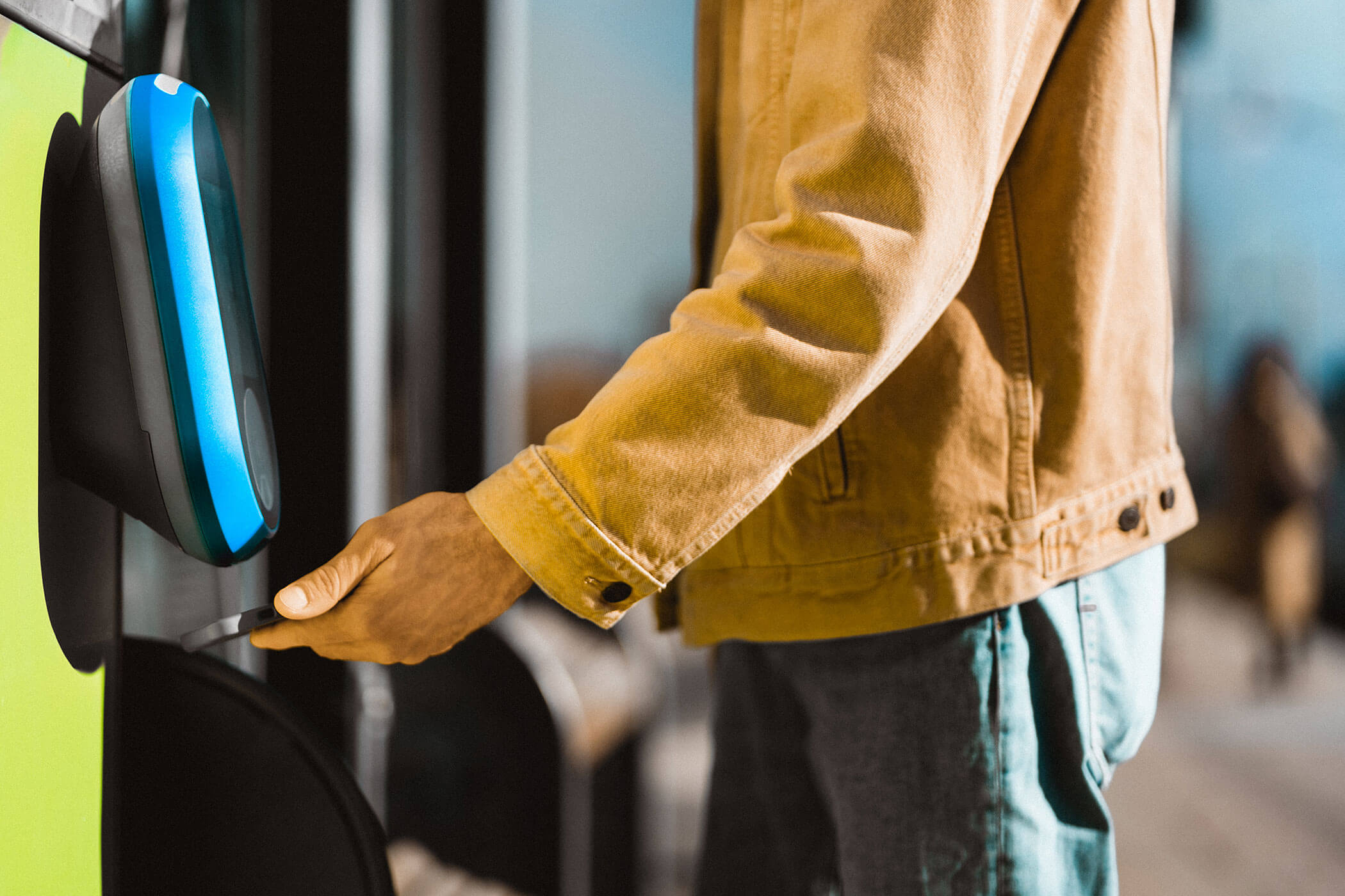 Eine Person in einer hellbraunen Jacke, die eine Karte in der Hand hält, neben einem kontaktlosen Bus-Bezahlterminal. - Hotel Oberwiesen