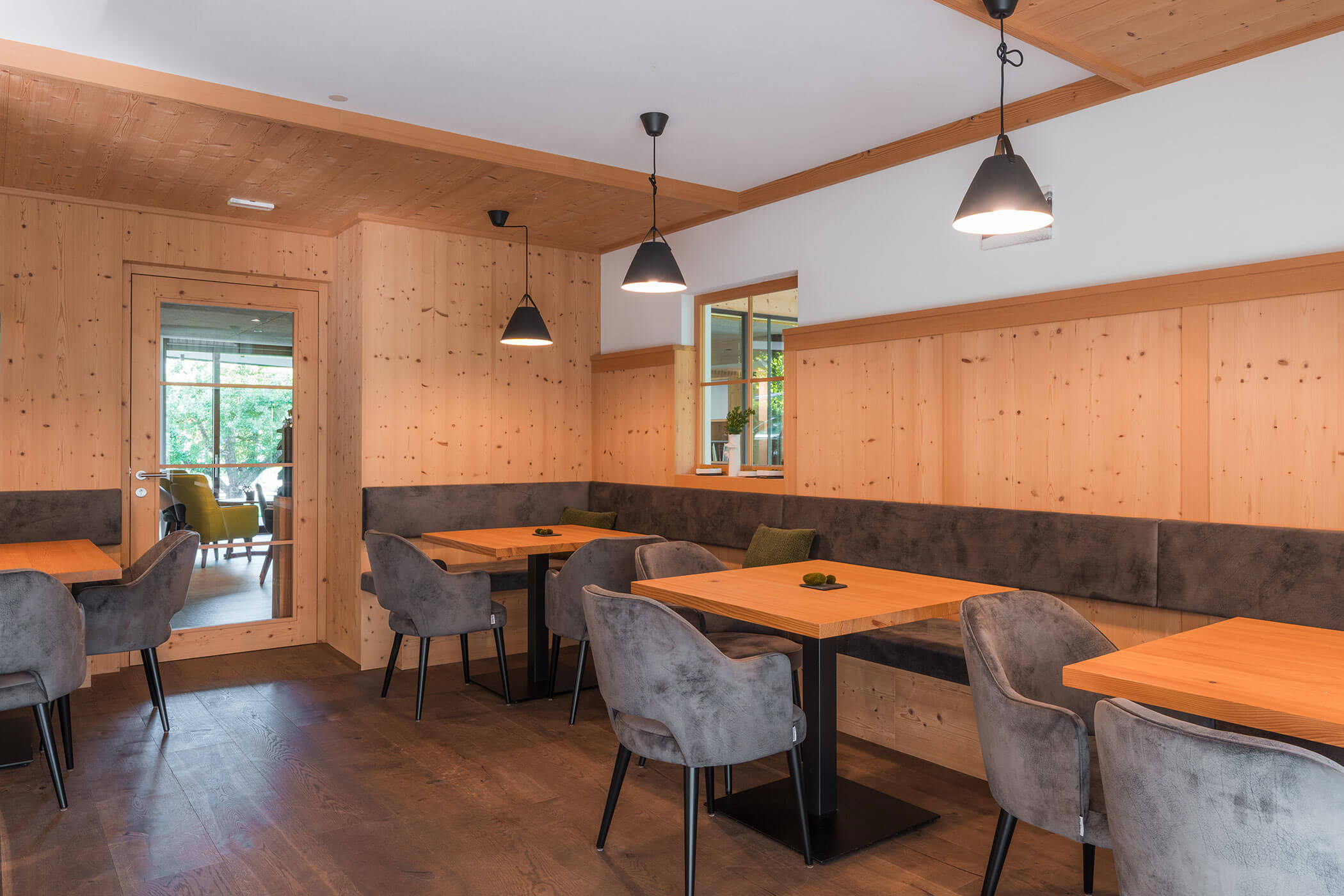 Moderner Essbereich mit Holzwänden, Tischen, grauen Stühlen und Pendelleuchten. - Hotel Oberwiesen