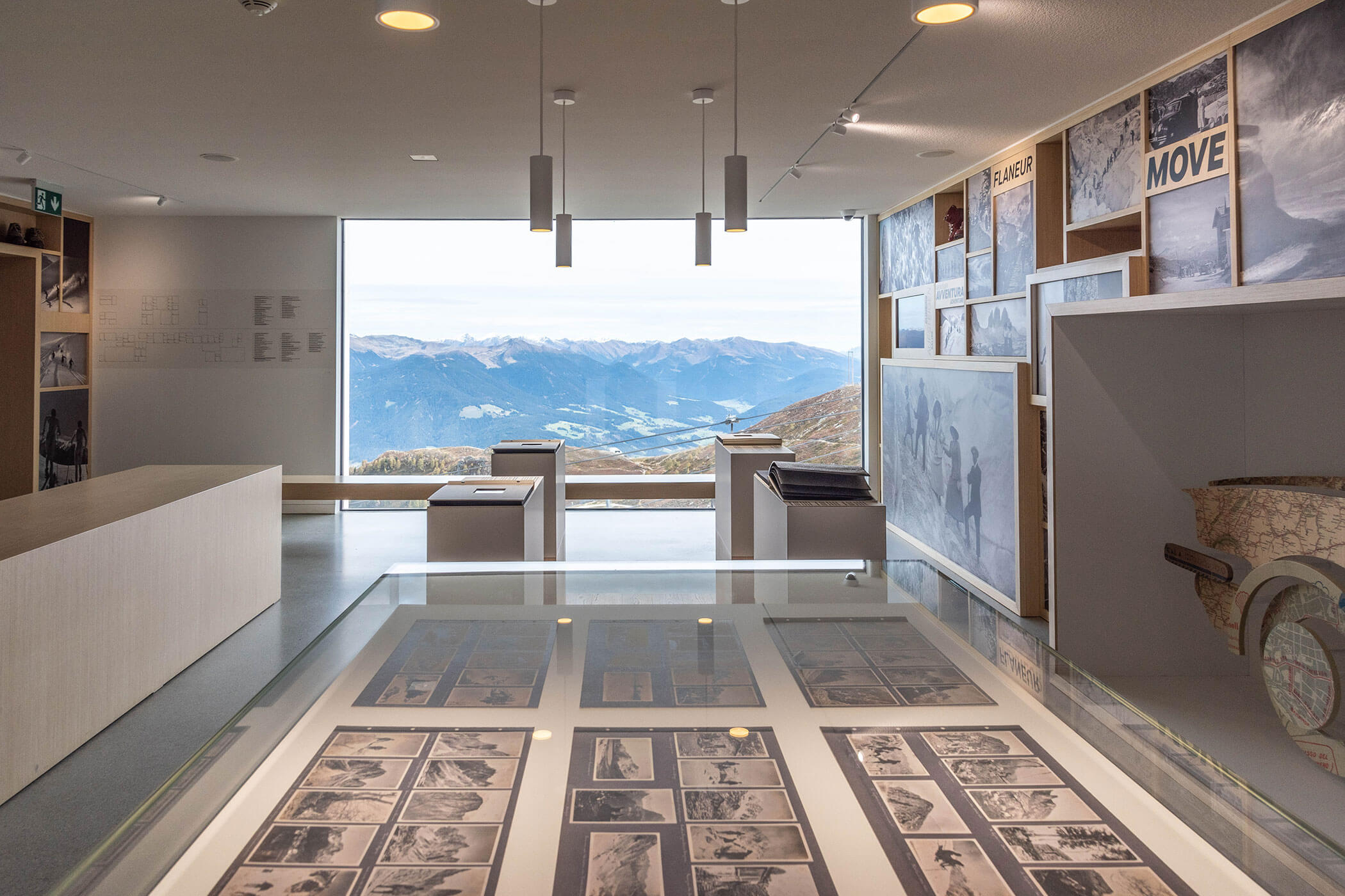 Sala museale moderna con esposizioni fotografiche e un'ampia finestra che offre una vista su un paesaggio montano sullo sfondo. - Hotel Oberwiesen