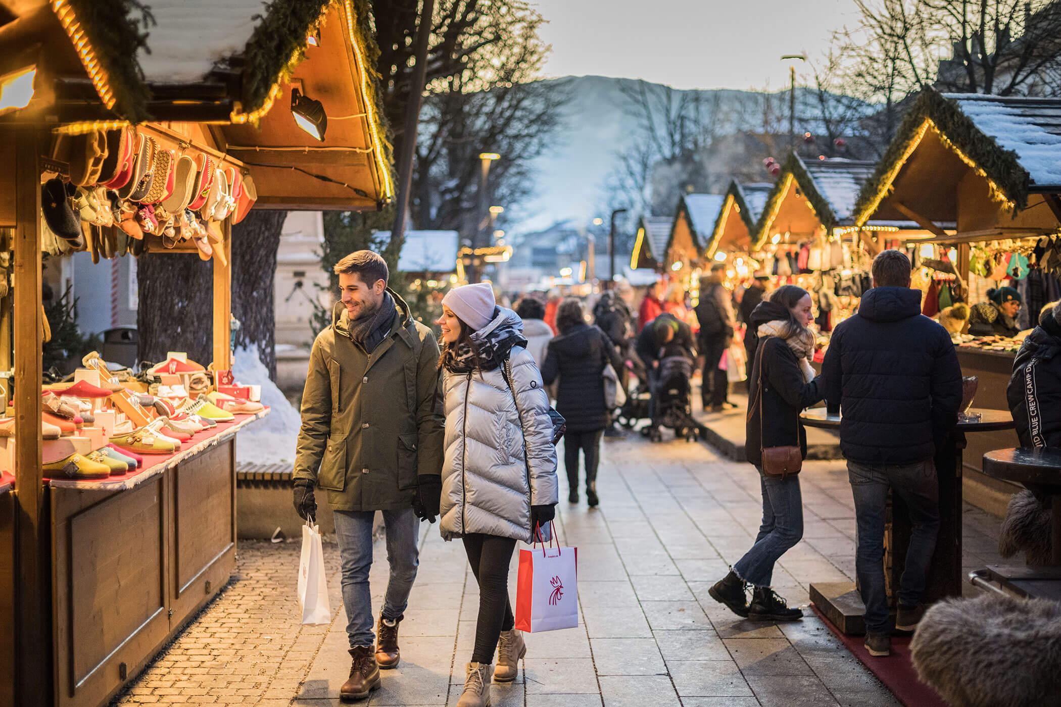 Una coppia fa acquisti in un mercatino invernale all’aperto, costellato di bancarelle di legno che vendono articoli da regalo e decorazioni. - Hotel Oberwiesen