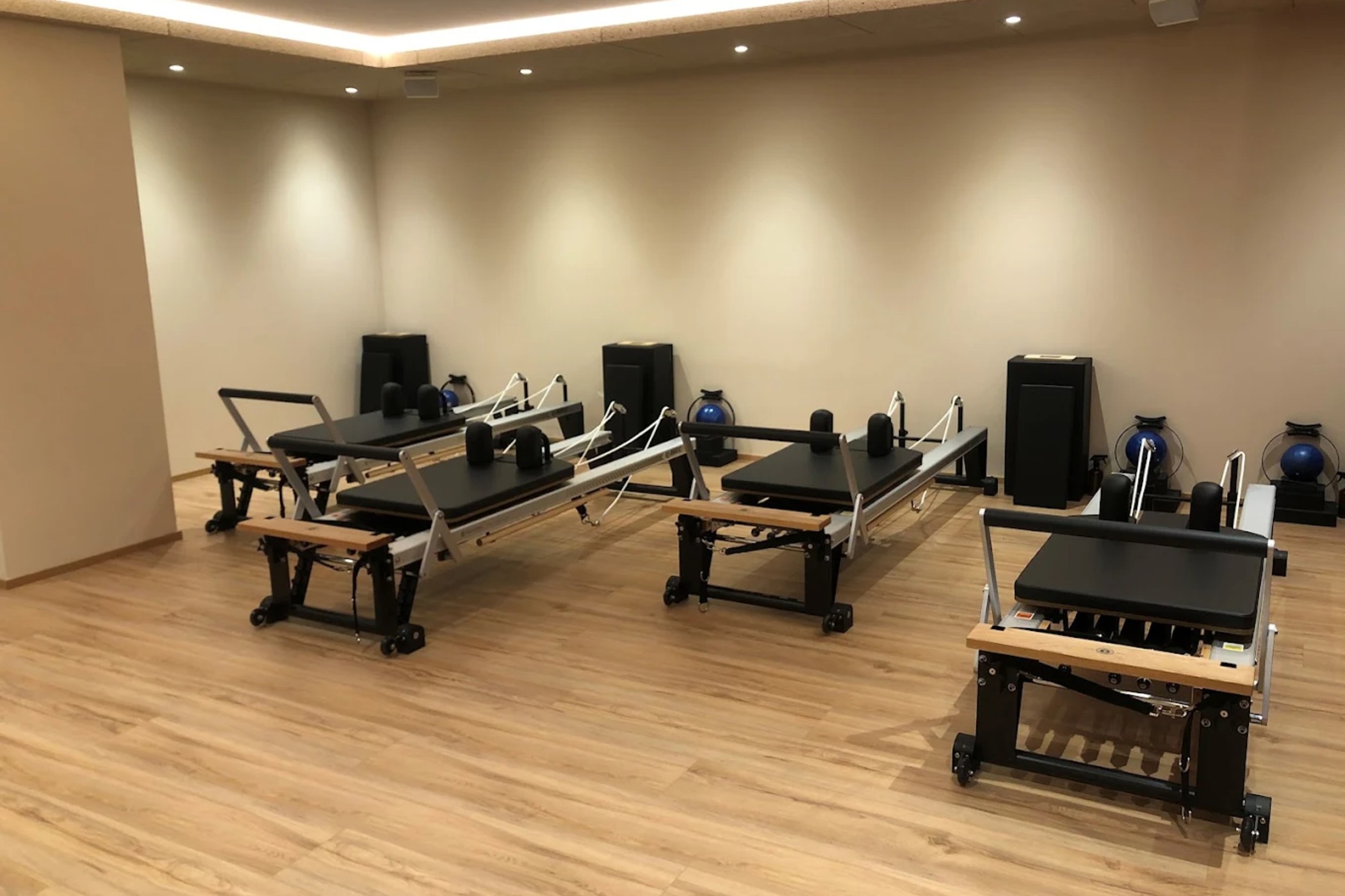 Pilates-Studio mit drei Reformer-Geräten auf einem Holzboden und Kettlebells an der Rückwand. - Hotel Oberwiesen