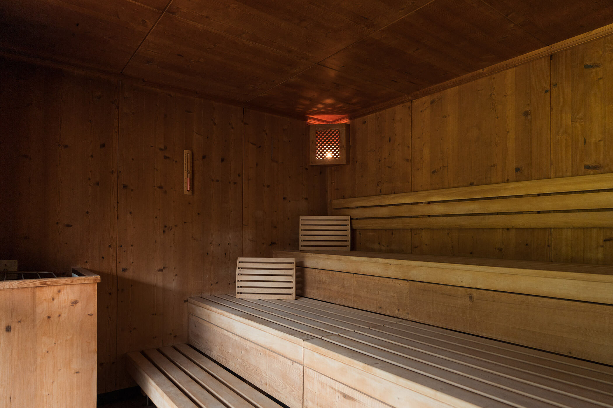 Eine leere Holzsauna mit gestuften Bänken und einem kleinen Licht, das in der oberen Ecke neben einer Lüftungsklappe leuchtet. - Hotel Oberwiesen