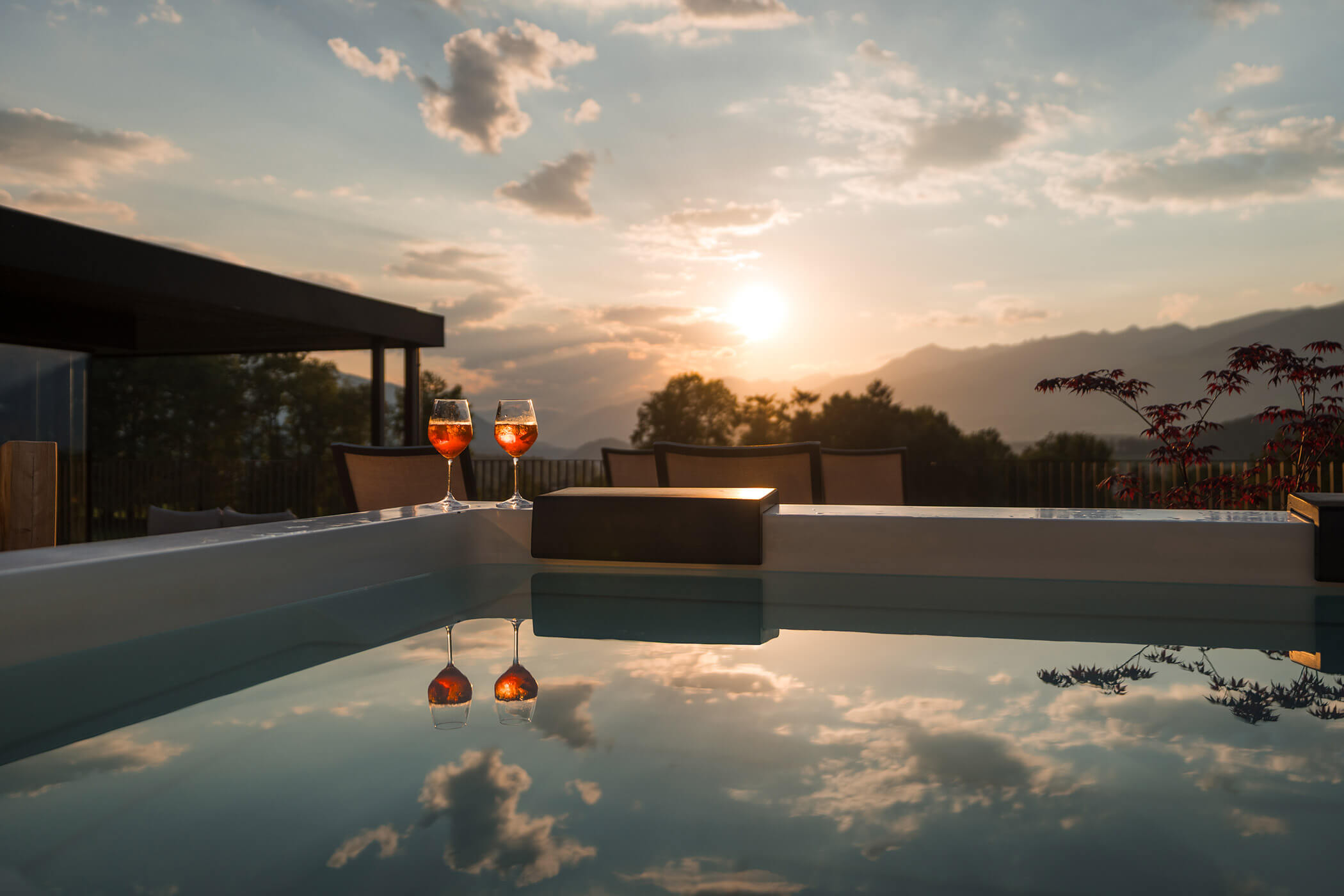 Zwei Gläser Wein am Pool bei Sonnenuntergang, während sich Berge und Wolken im Wasser spiegeln. - Hotel Oberwiesen