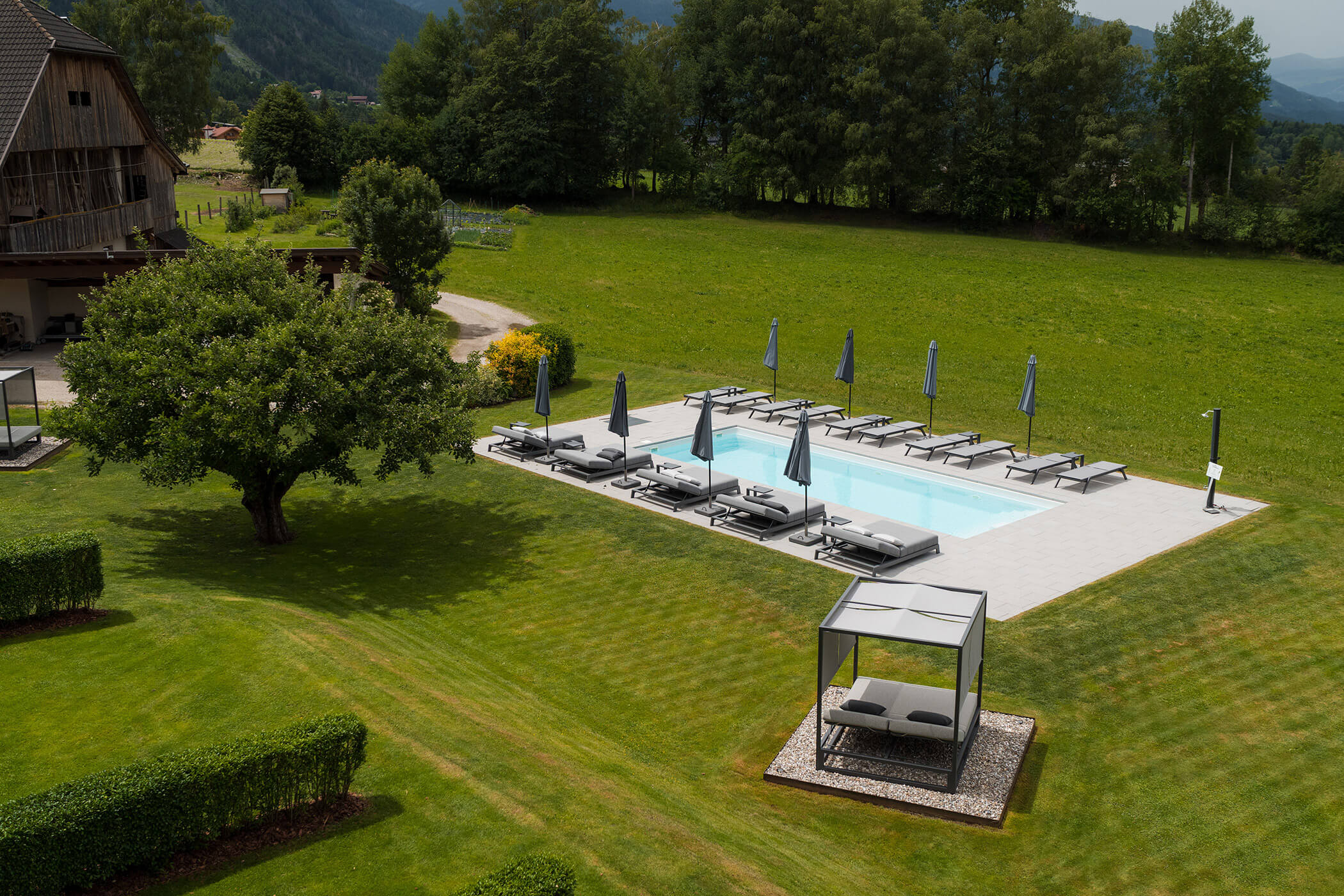In einem grünen Garten mit Bäumen und einem schattigen Liegestuhlbereich befindet sich ein Pool mit Liegestühlen und Sonnenschirmen. - Hotel Oberwiesen