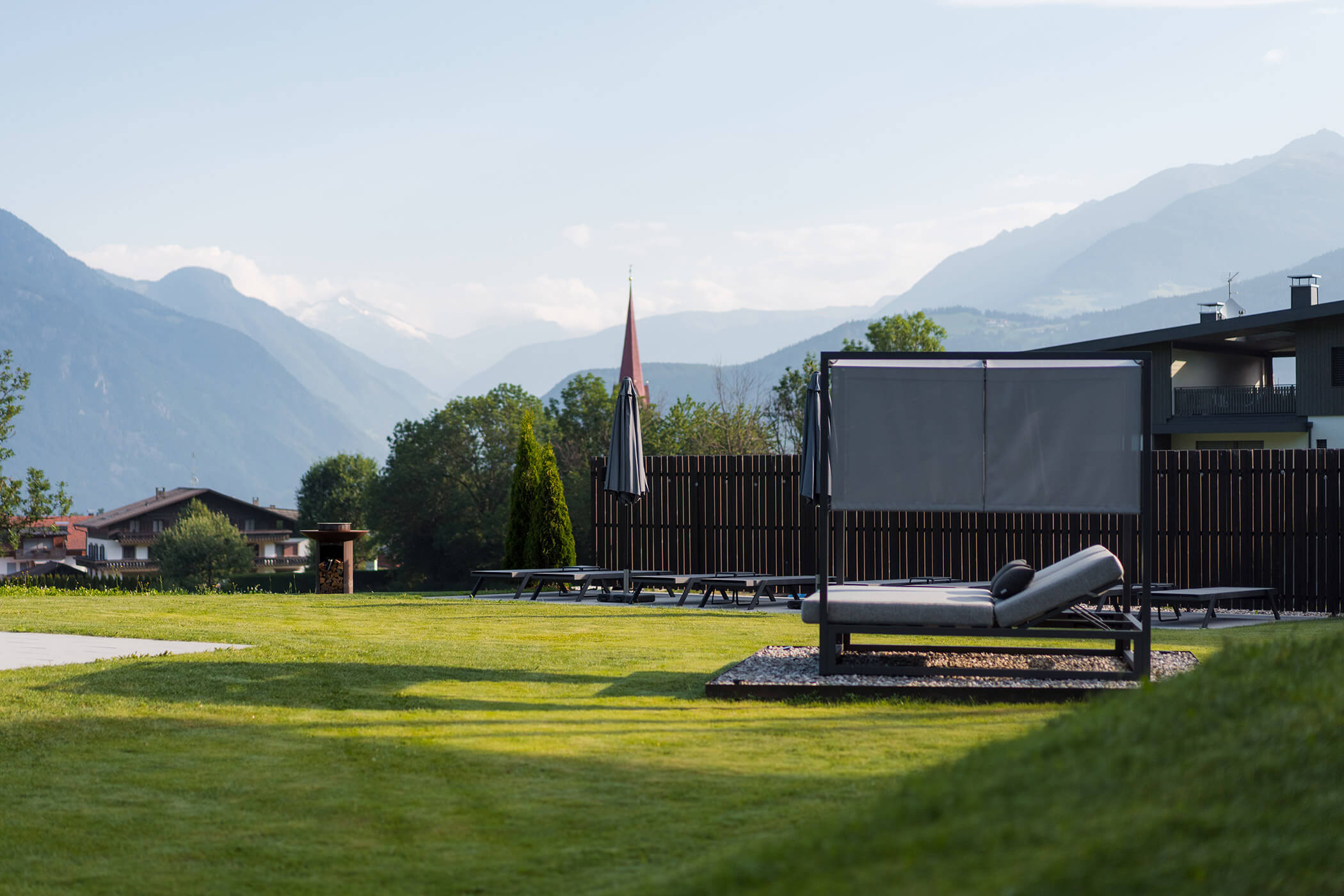 Ein Liegestuhl auf einer Rasenfläche mit Bergen und Gebäuden im Hintergrund unter einem klaren Himmel. - Hotel Oberwiesen
