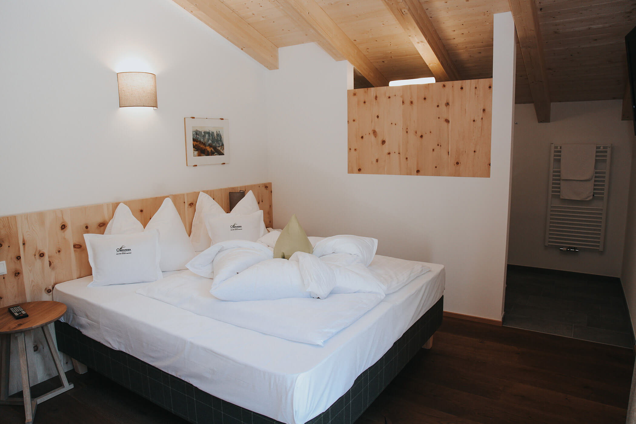 Accogliente camera da letto con letto matrimoniale, biancheria da letto bianca, dettagli in legno e un portasciugamani a muro. - Hotel Oberwiesen