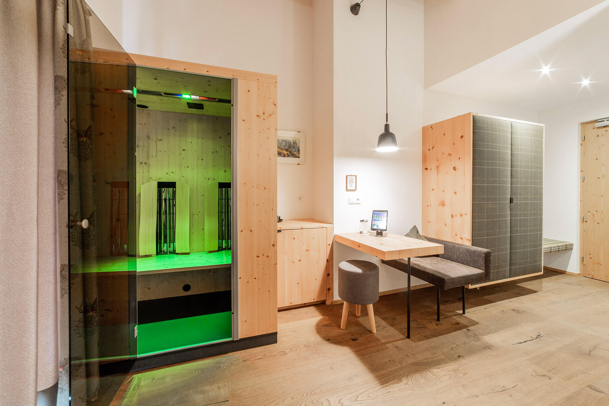 Camera moderna con mobili in legno, una piccola zona pranzo e una sauna in vetro illuminata da luci verdi. - Hotel Oberwiesen