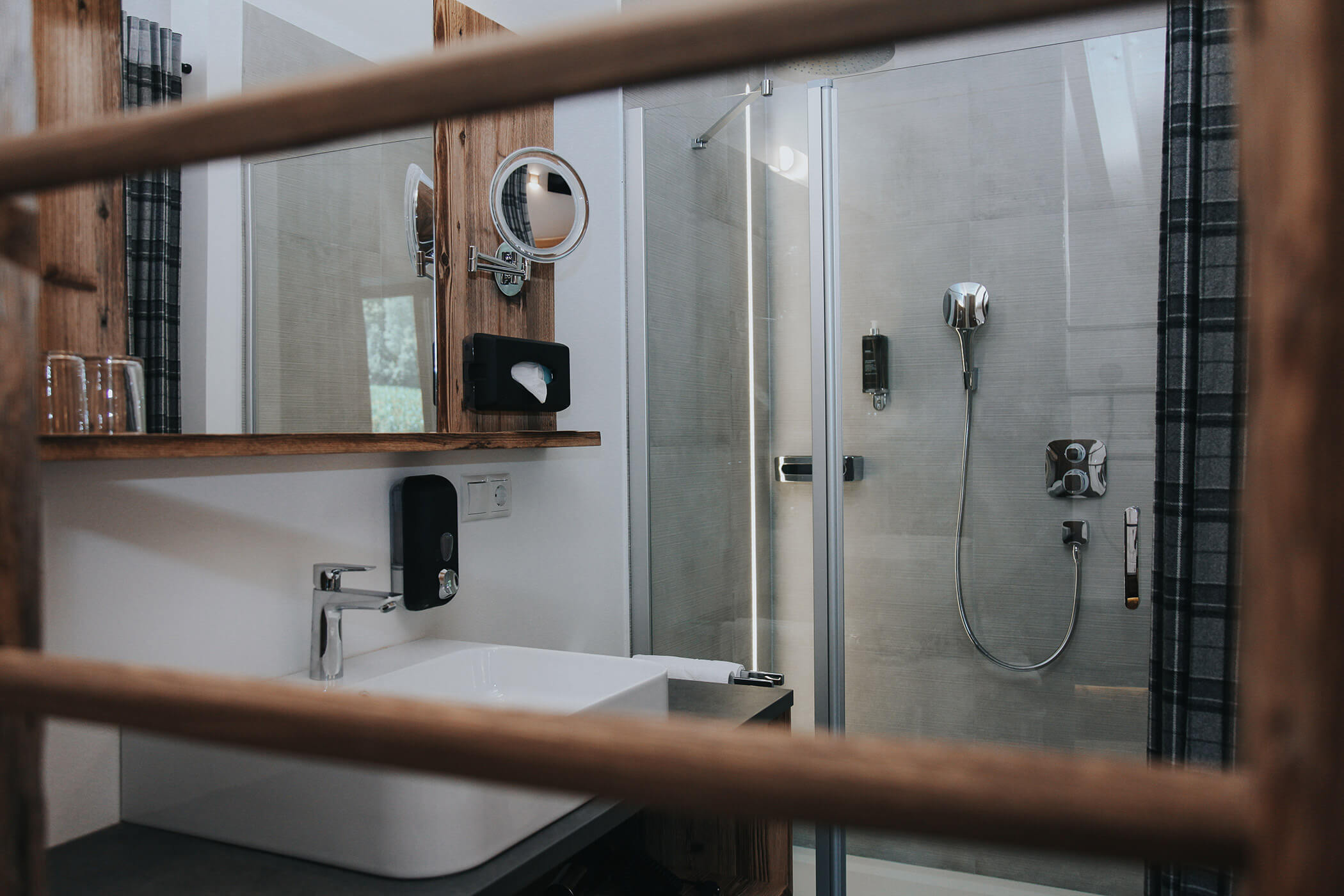 Bagno moderno con dettagli in legno, lavabo, specchio e box doccia in vetro con accessori. - Hotel Oberwiesen