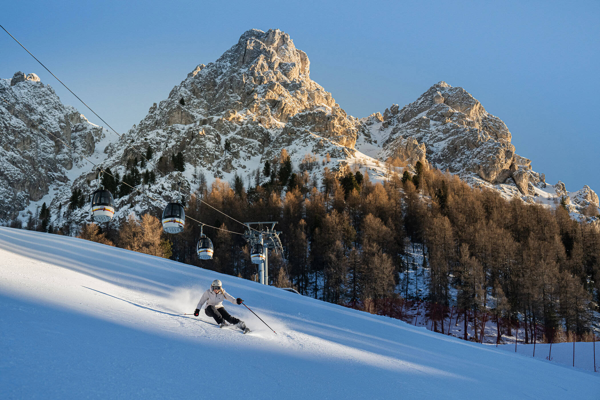 Ein Skifahrer fährt unter klarem Himmel einen verschneiten Hang hinunter, im Hintergrund sind ein Skilift und felsige Berggipfel zu sehen. - Hotel Oberwiesen