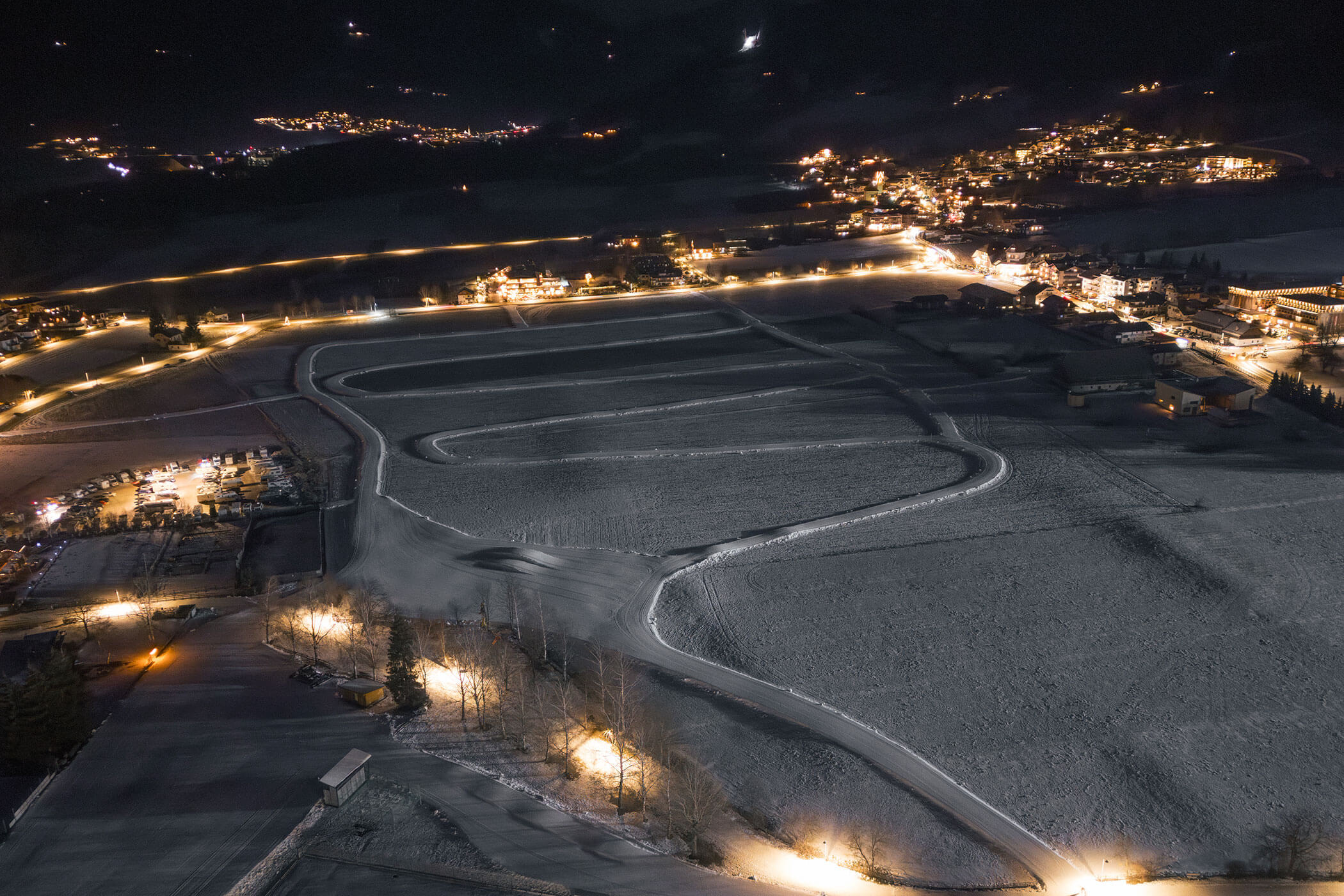Verschneite Landschaft mit gewundenen Wegen, beleuchtet von Straßenlaternen, umgeben von Gebäuden bei Nacht. - Hotel Oberwiesen